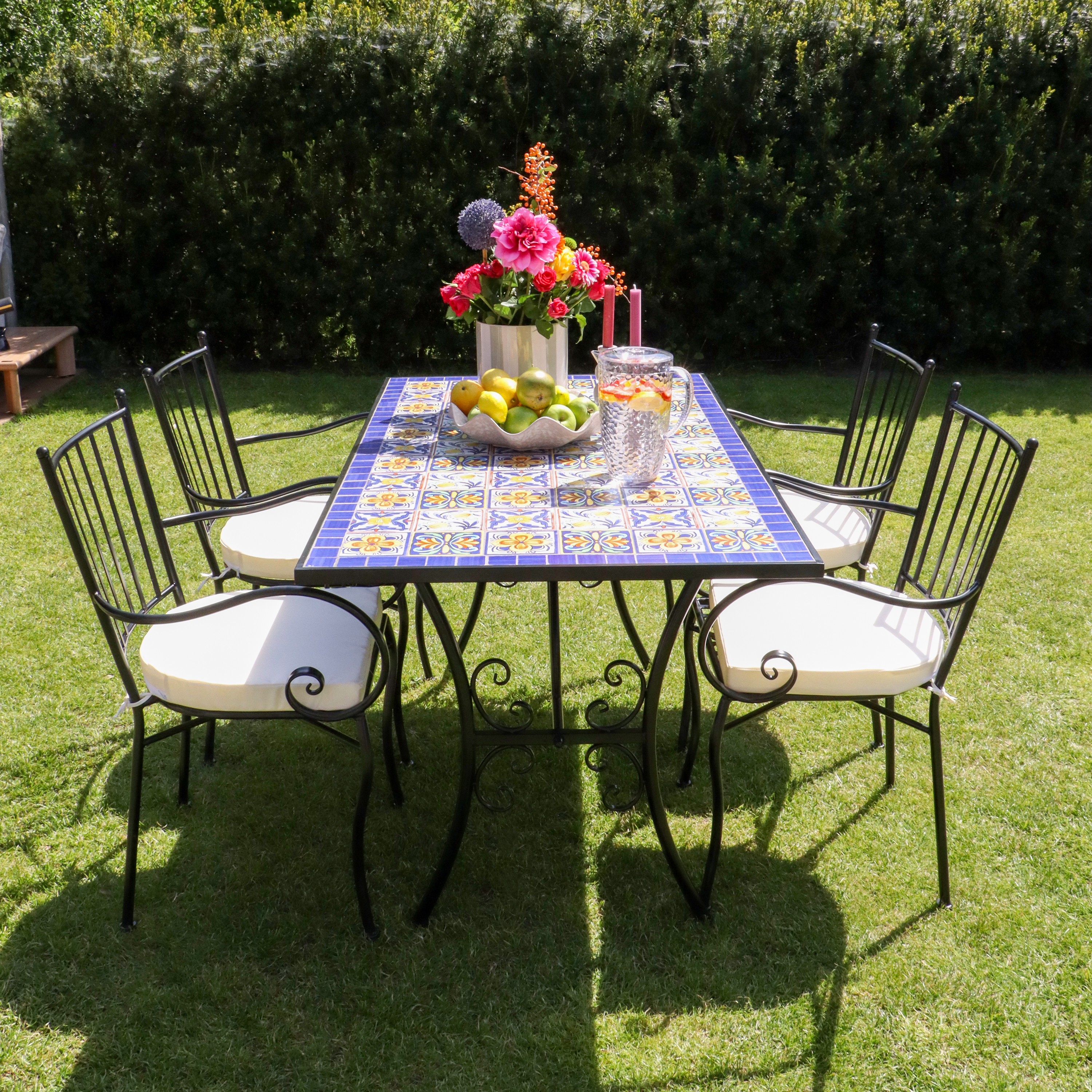 Ein Gartentisch mit Blumen, Obst und Getränken, umgeben von vier Stühlen auf einem Rasen.