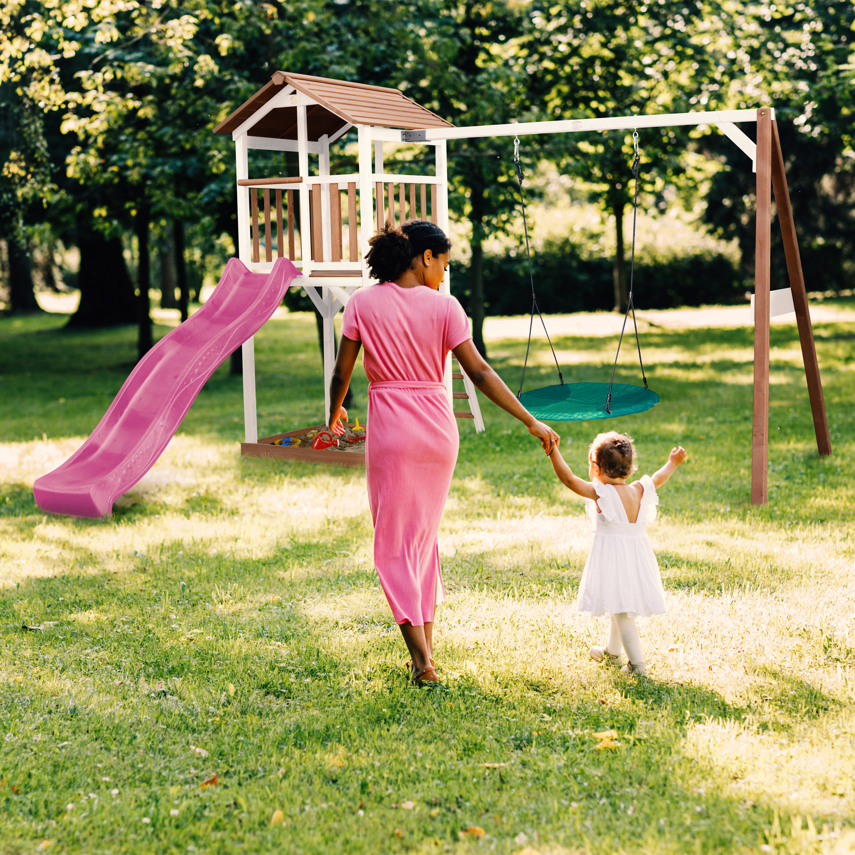 Mutter und Kind gehen auf einem Spielplatz mit Rutsche und Schaukel.