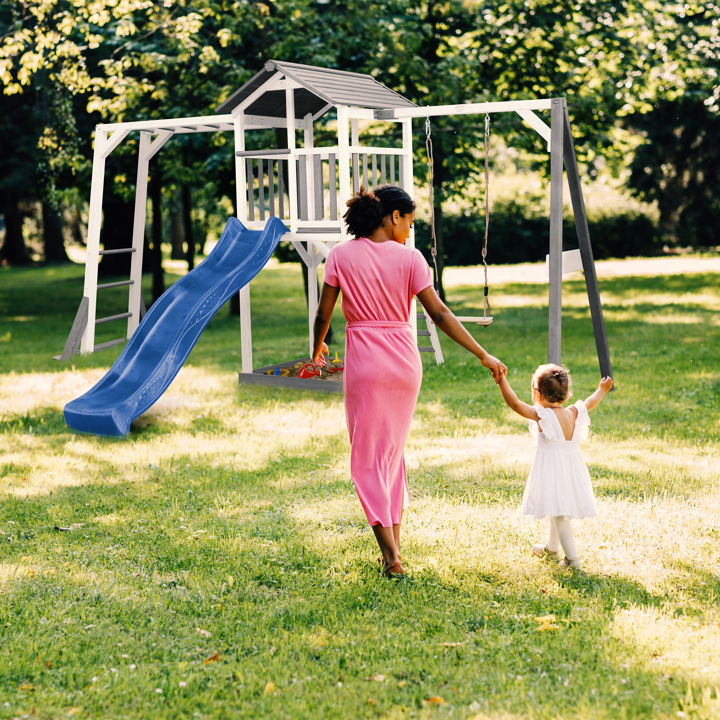 Mutter und Kind gehen auf einen Spielplatz mit Rutsche und Schaukel im Park.