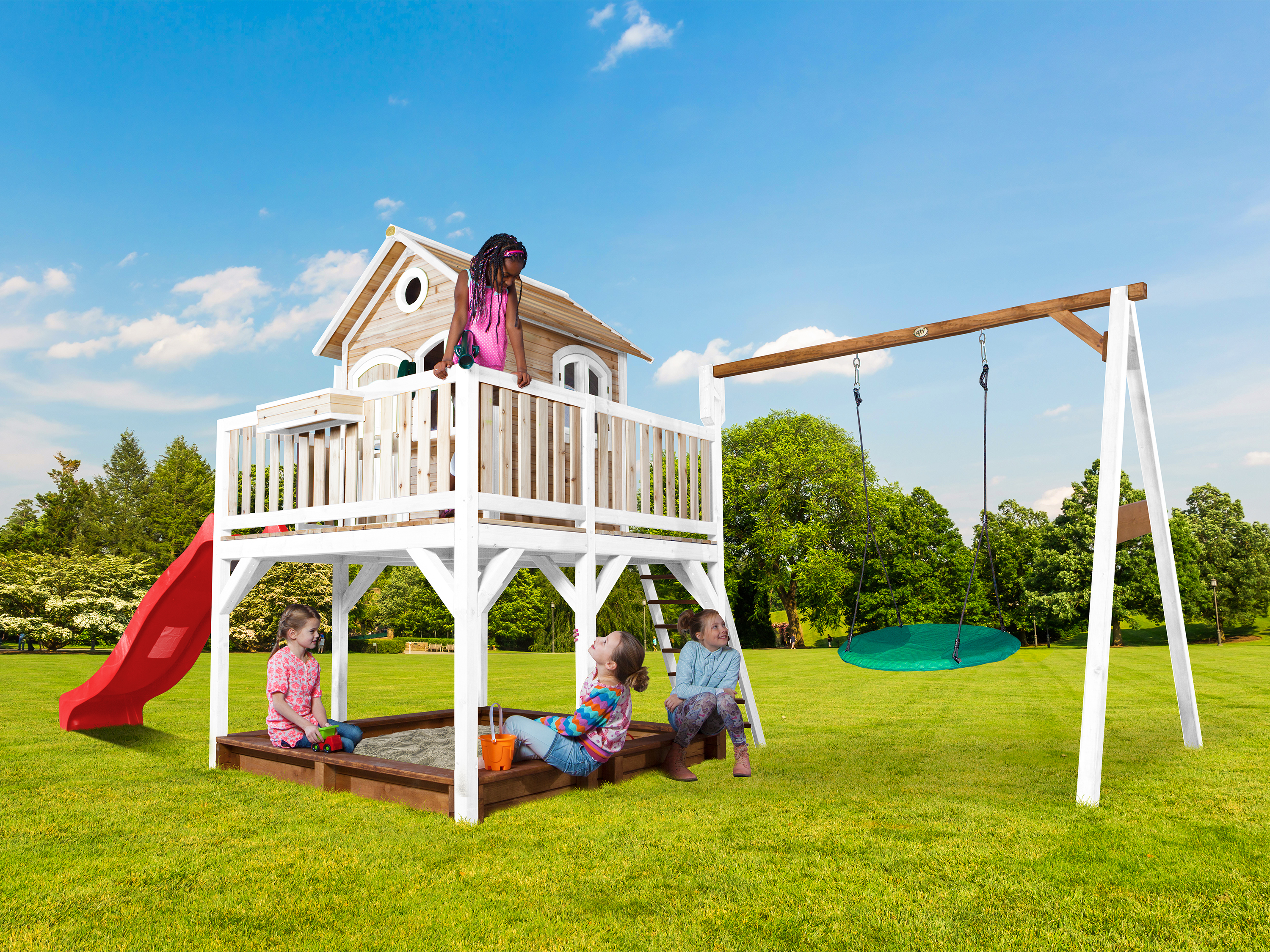 Kinder spielen auf einem Spielgerät mit Rutsche, Sandkasten und Schaukel.