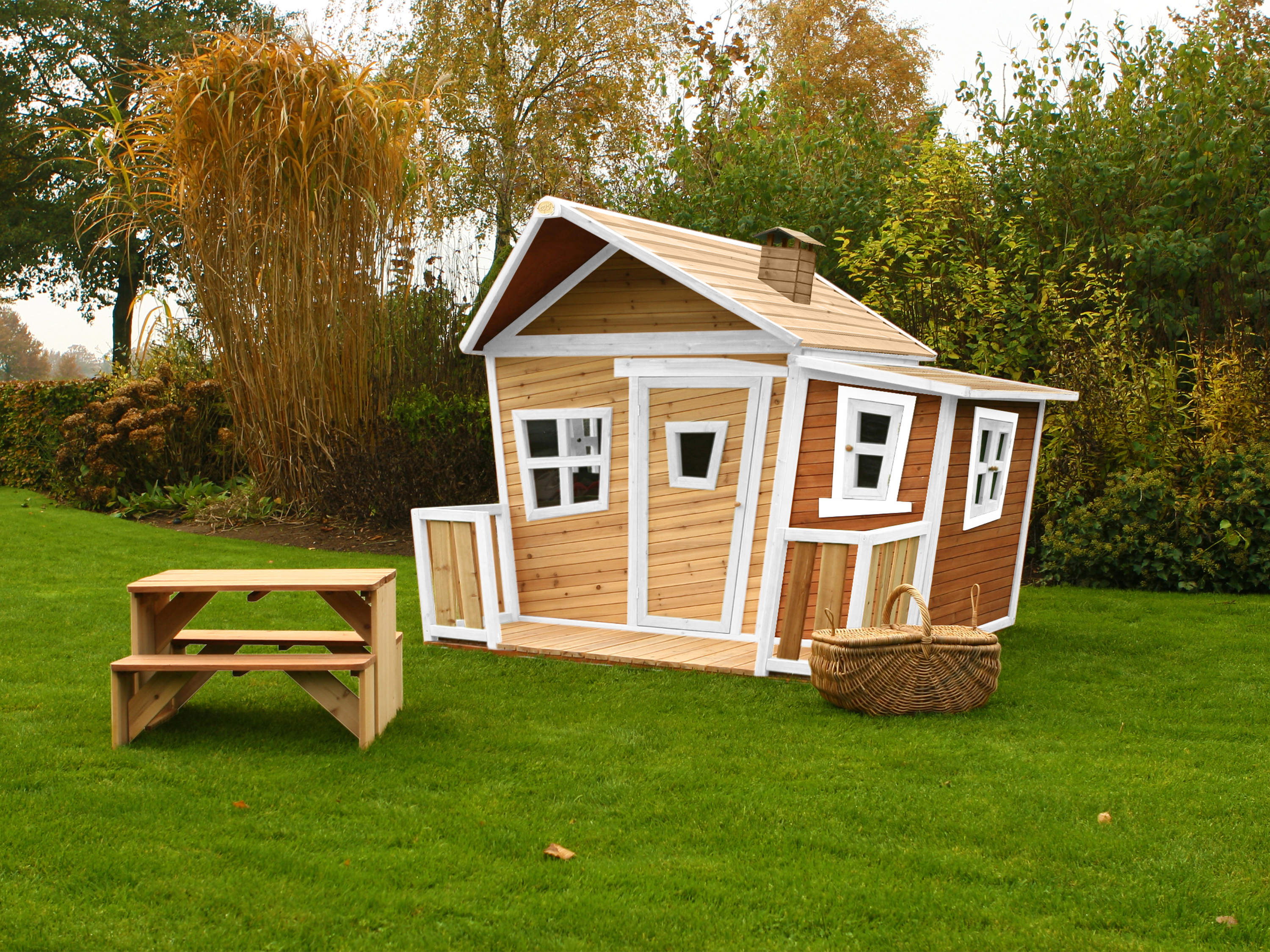 Ein hölzernes Spielhaus steht auf einem Rasen mit einem Picknicktisch und einem Korb.