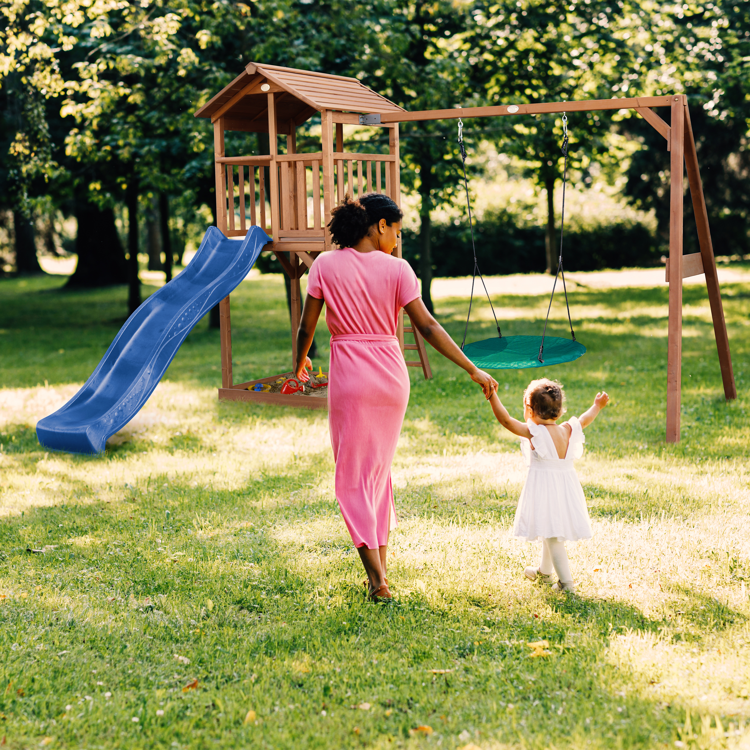 Mutter und Kind gehen zu einem Spielplatz mit Rutsche und Schaukel im Park.