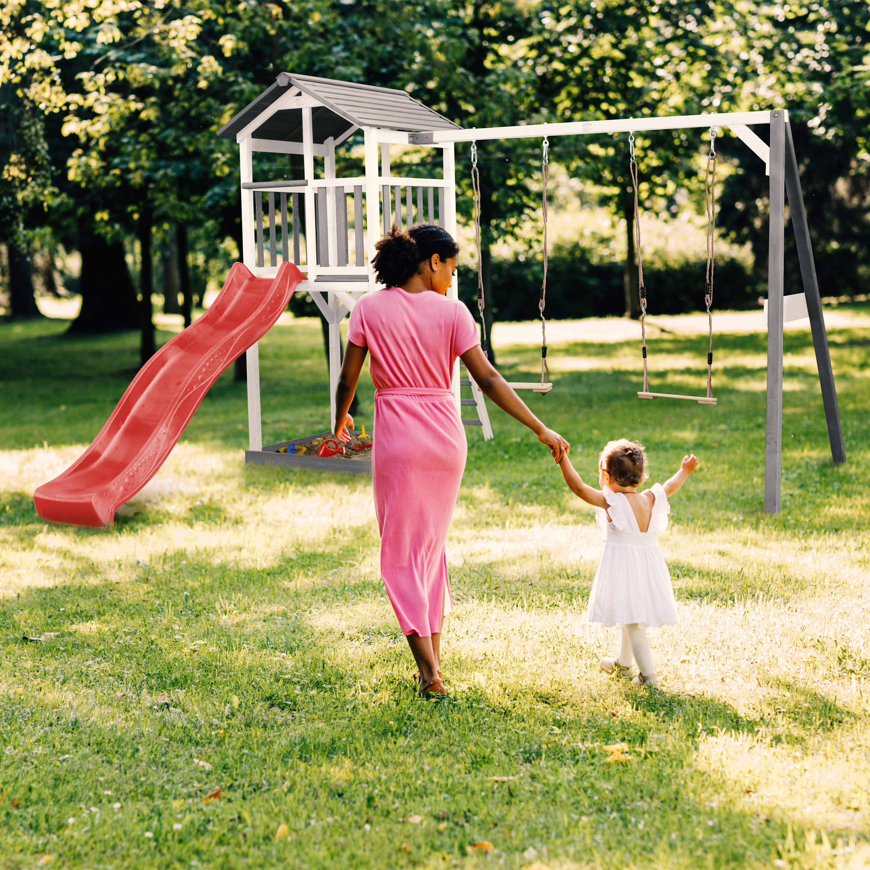 Mutter und Kind gehen zum Spielplatz mit Rutsche und Schaukeln.