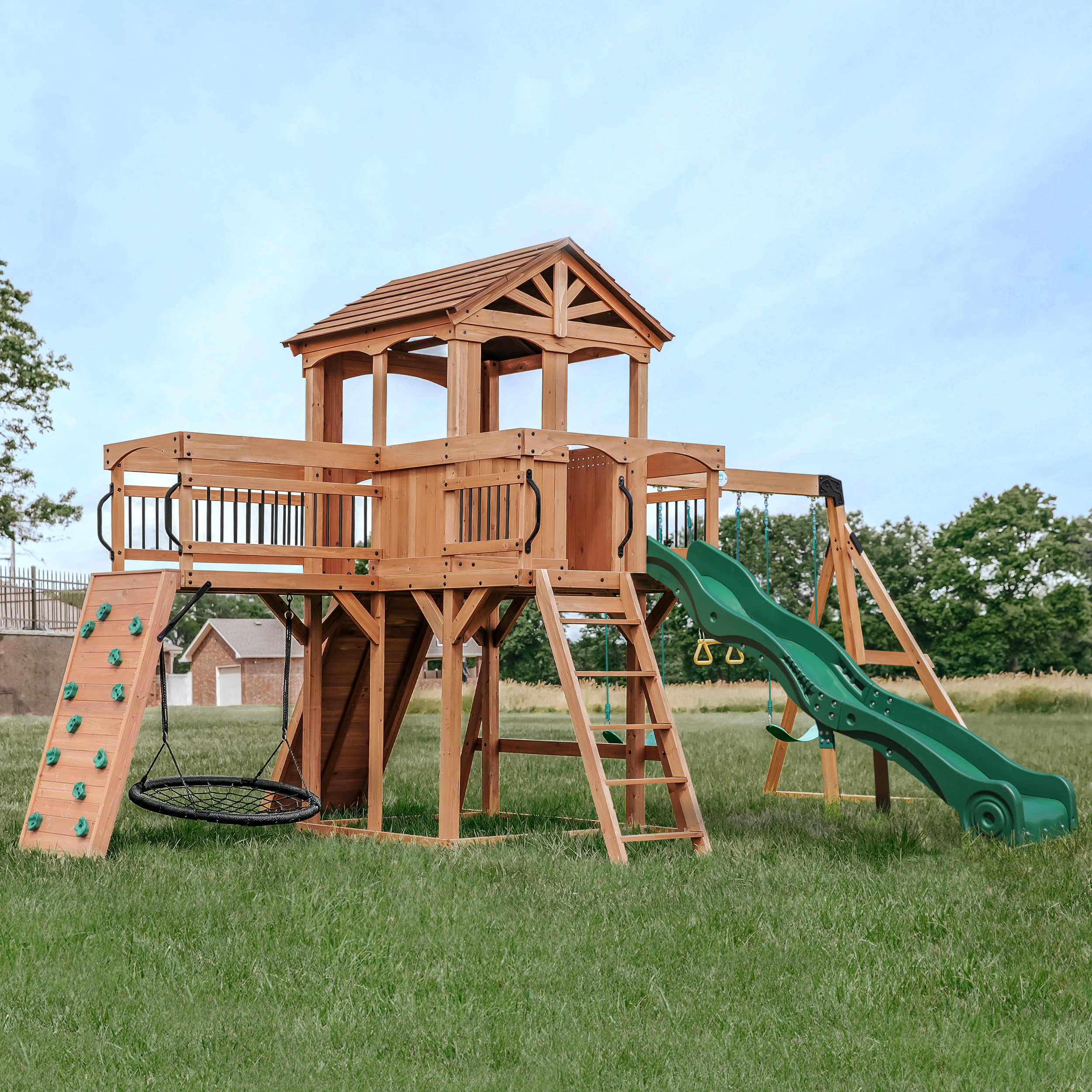 Ein hölzerner Spielturm mit Rutsche, Schaukeln und Kletterwand auf grünem Gras.