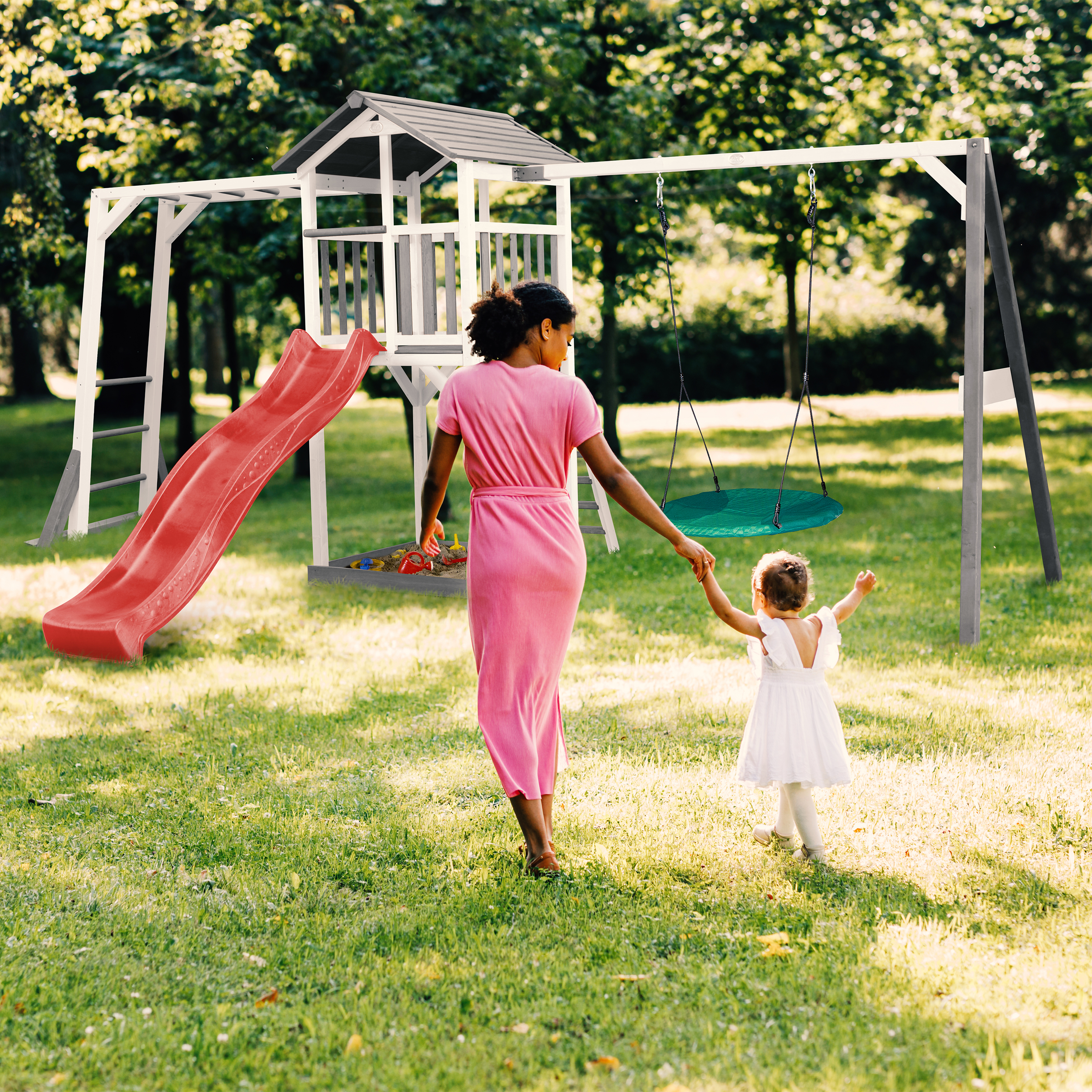 Frau und Kind gehen auf einem Spielplatz mit Rutsche und Schaukel.