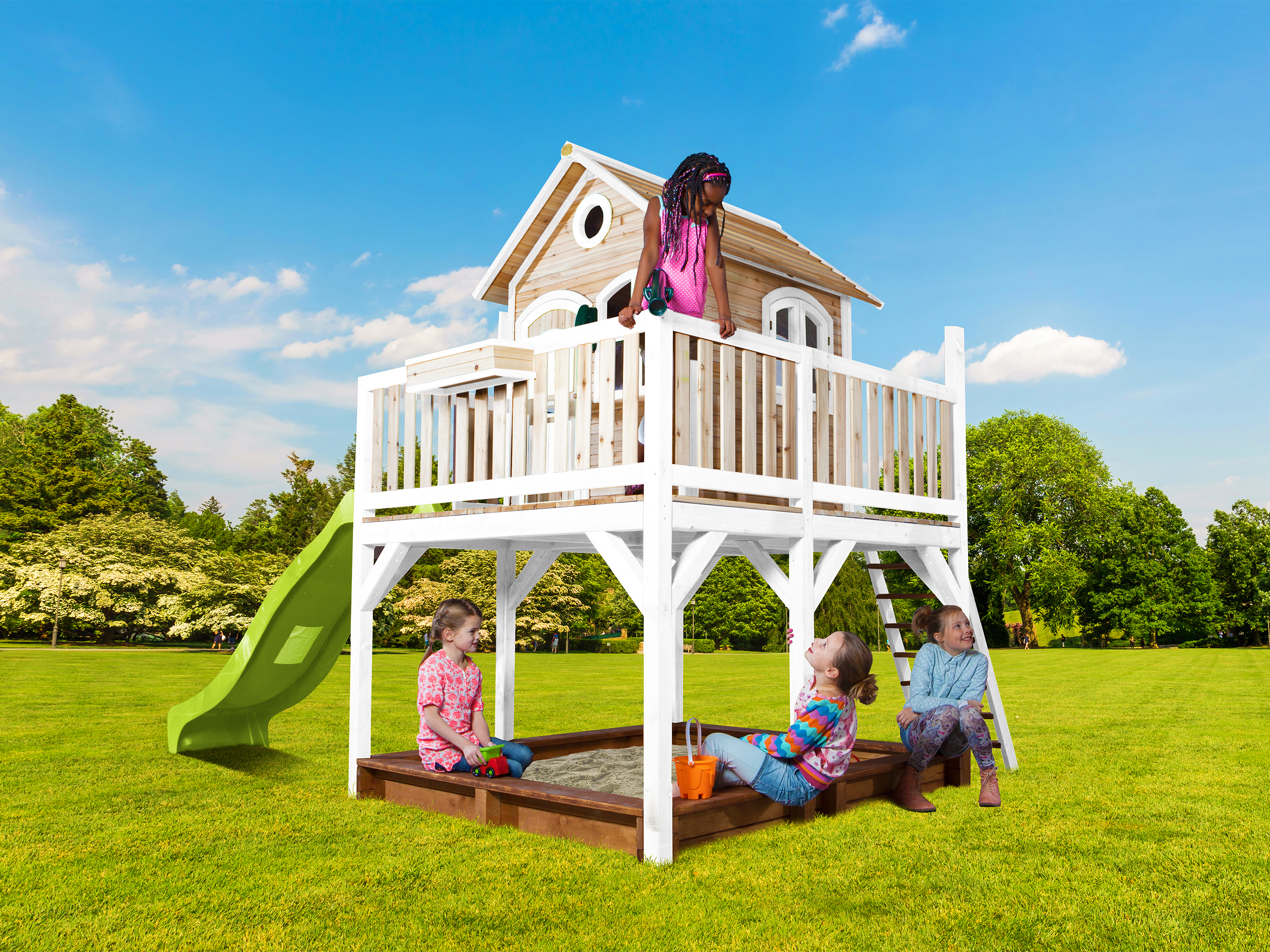 Kinder spielen auf einem Baumhaus mit Rutsche und Sandkasten an einem sonnigen Tag.
