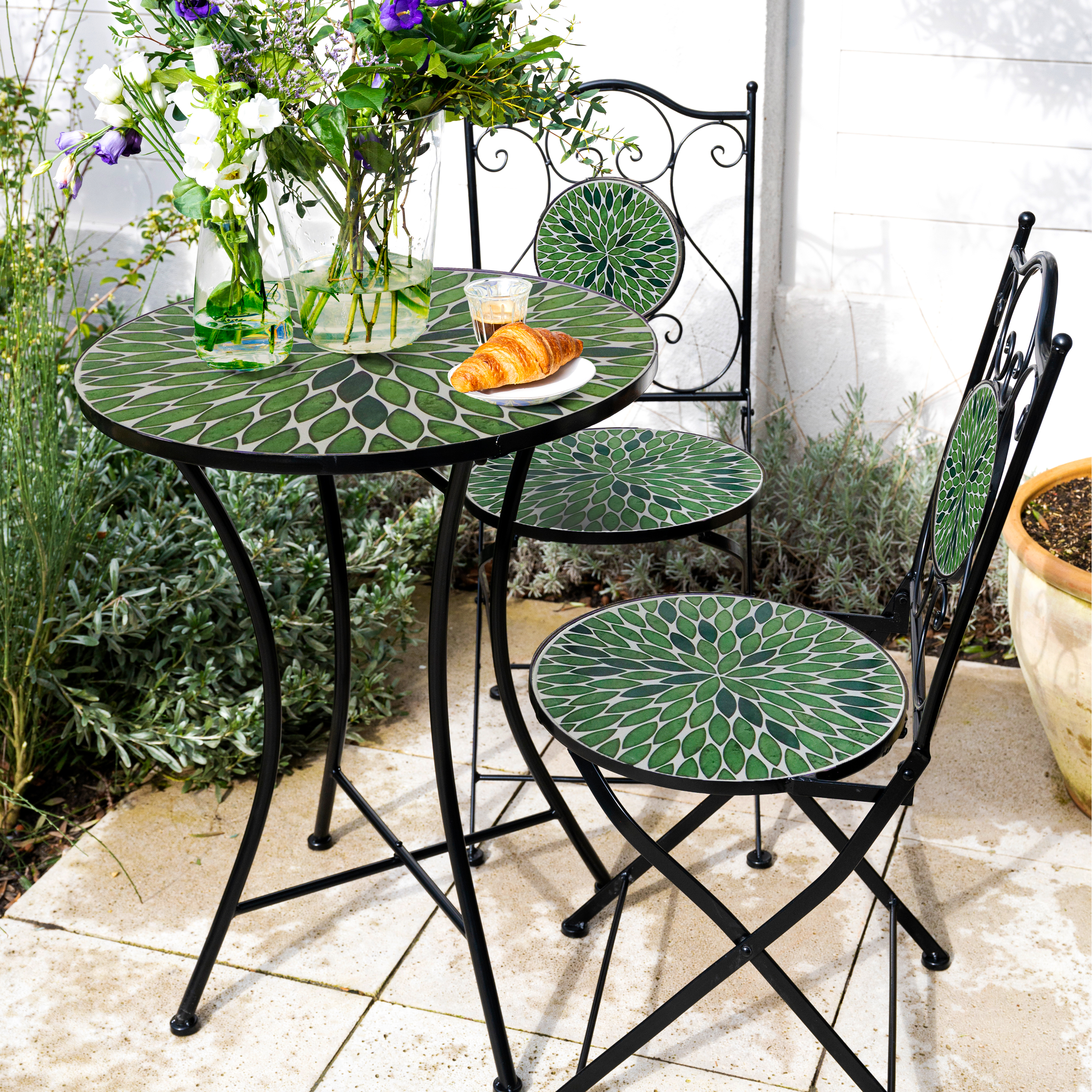Ein runder Tisch und zwei Stühle mit grünen Mosaikmustern auf einer Terrasse.