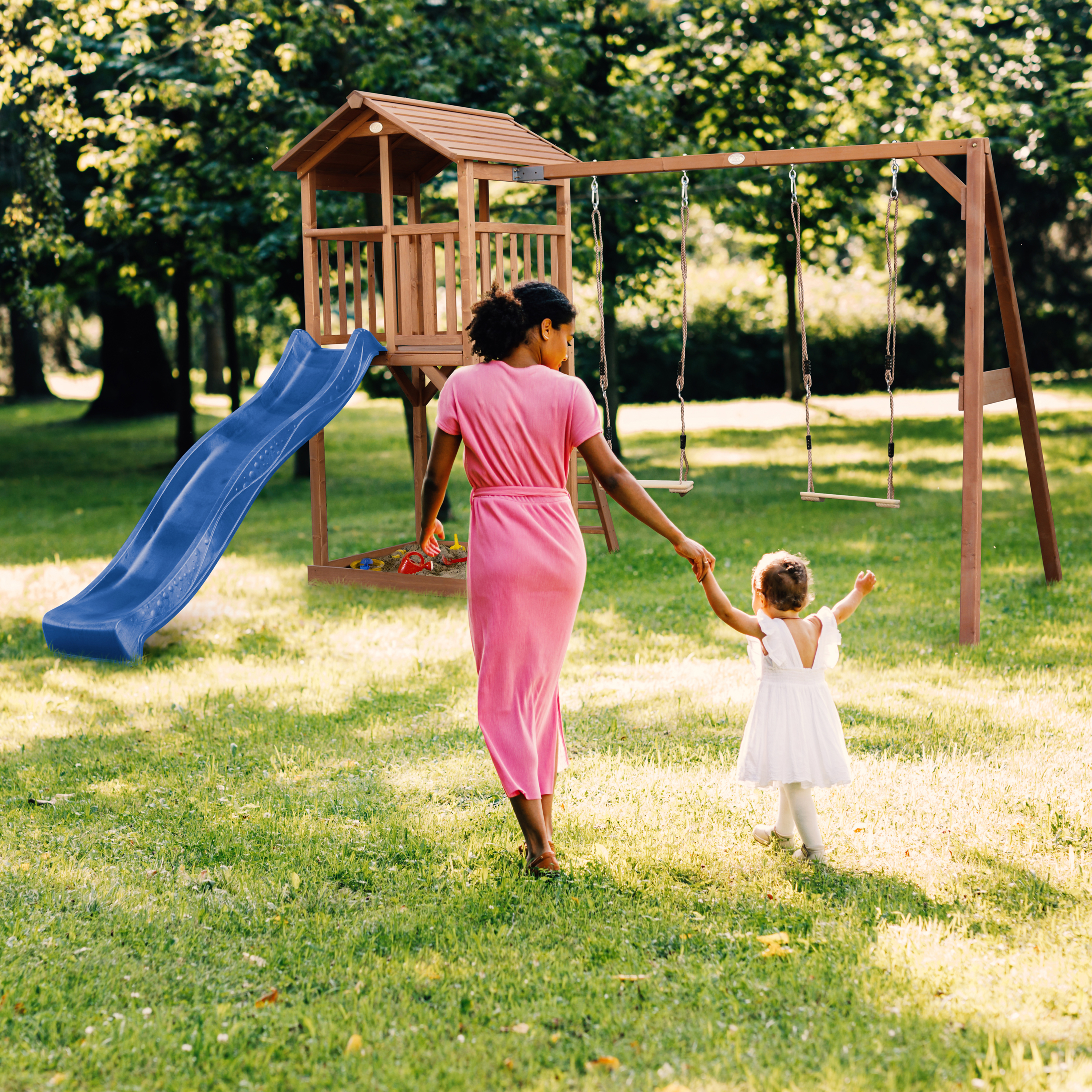 Mutter und Kind gehen zum Spielturm mit Rutsche und Schaukeln im Park.