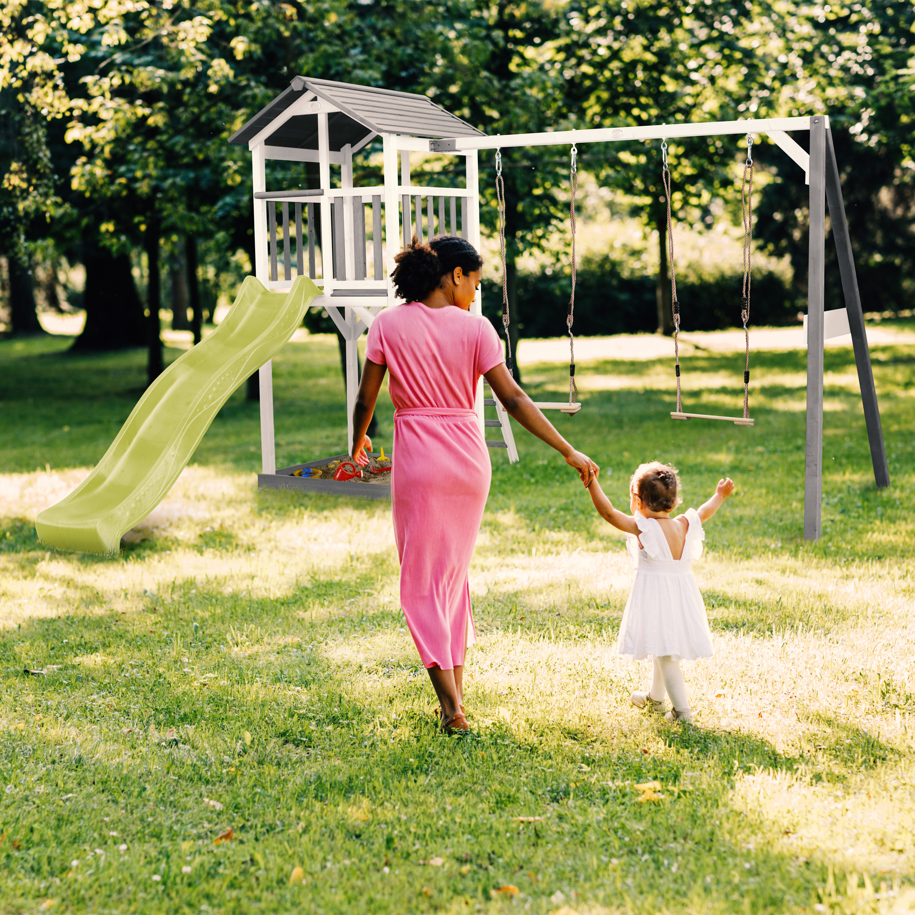 Mutter mit Kind gehen zum Spielplatz mit Rutsche und Schaukeln im Park.