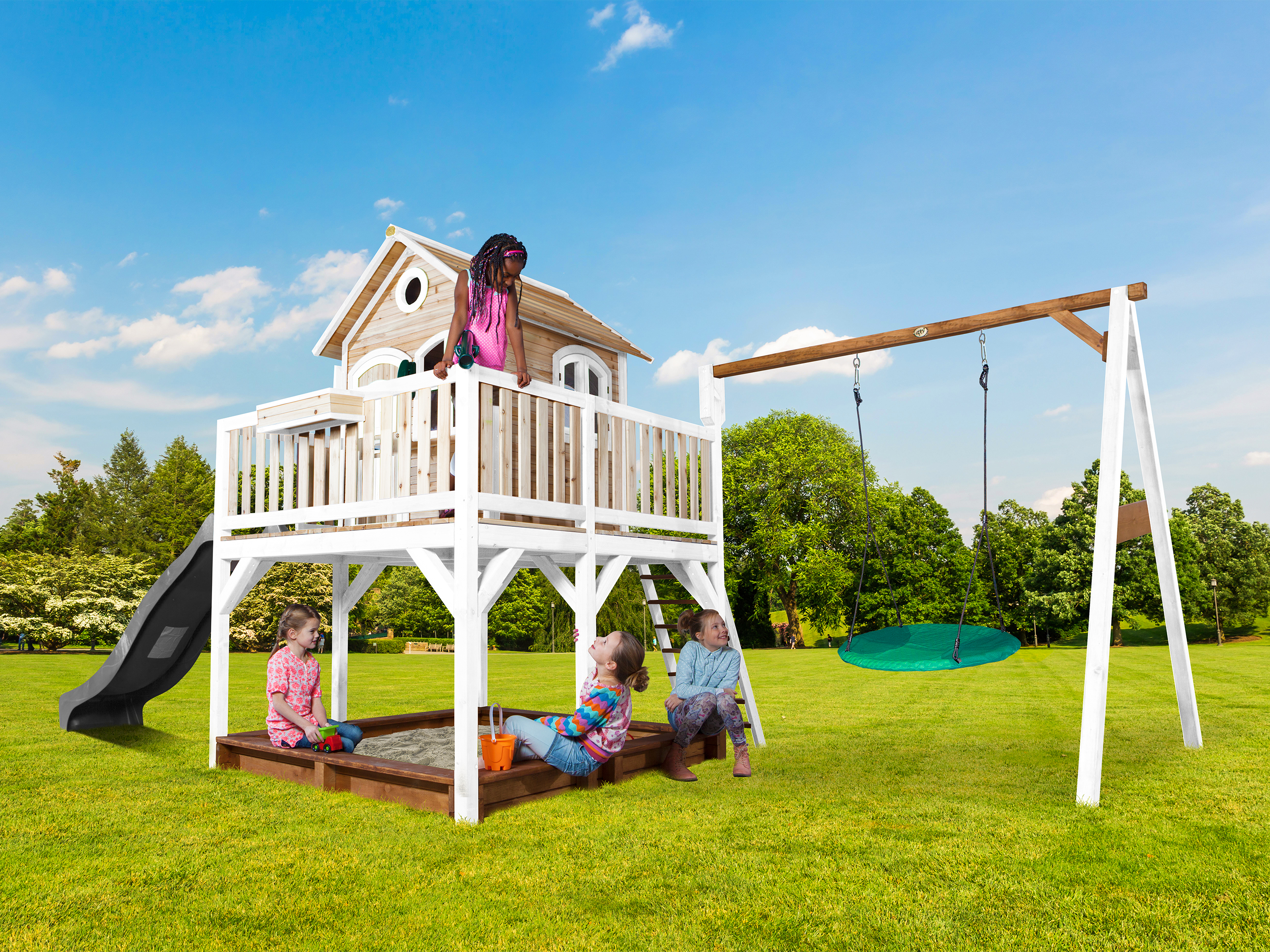 Kinder spielen auf einem Spielgerät mit Rutsche, Schaukel und Sandkasten im Garten.