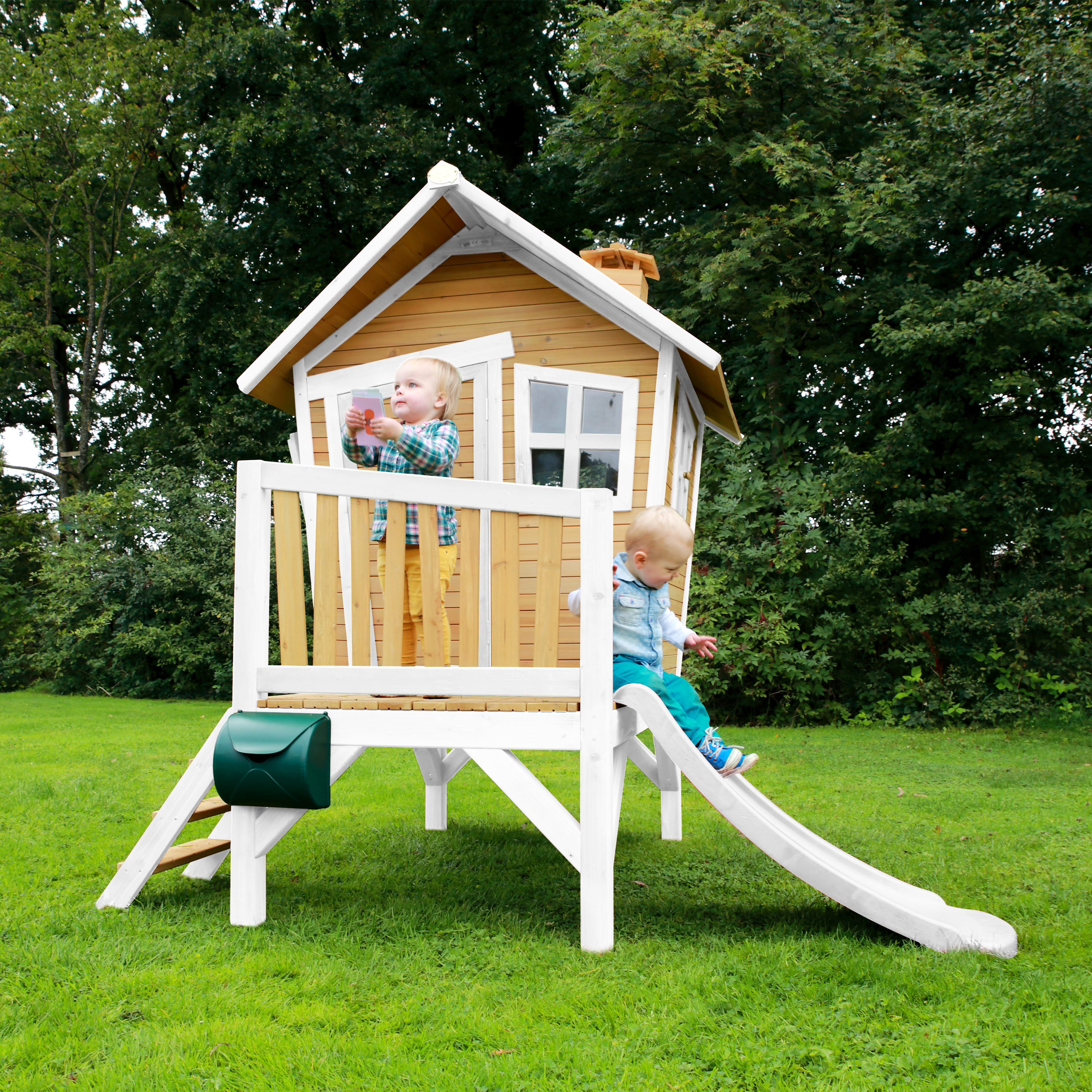 Zwei Kinder spielen auf einem Holzhaus mit Rutsche im Garten.