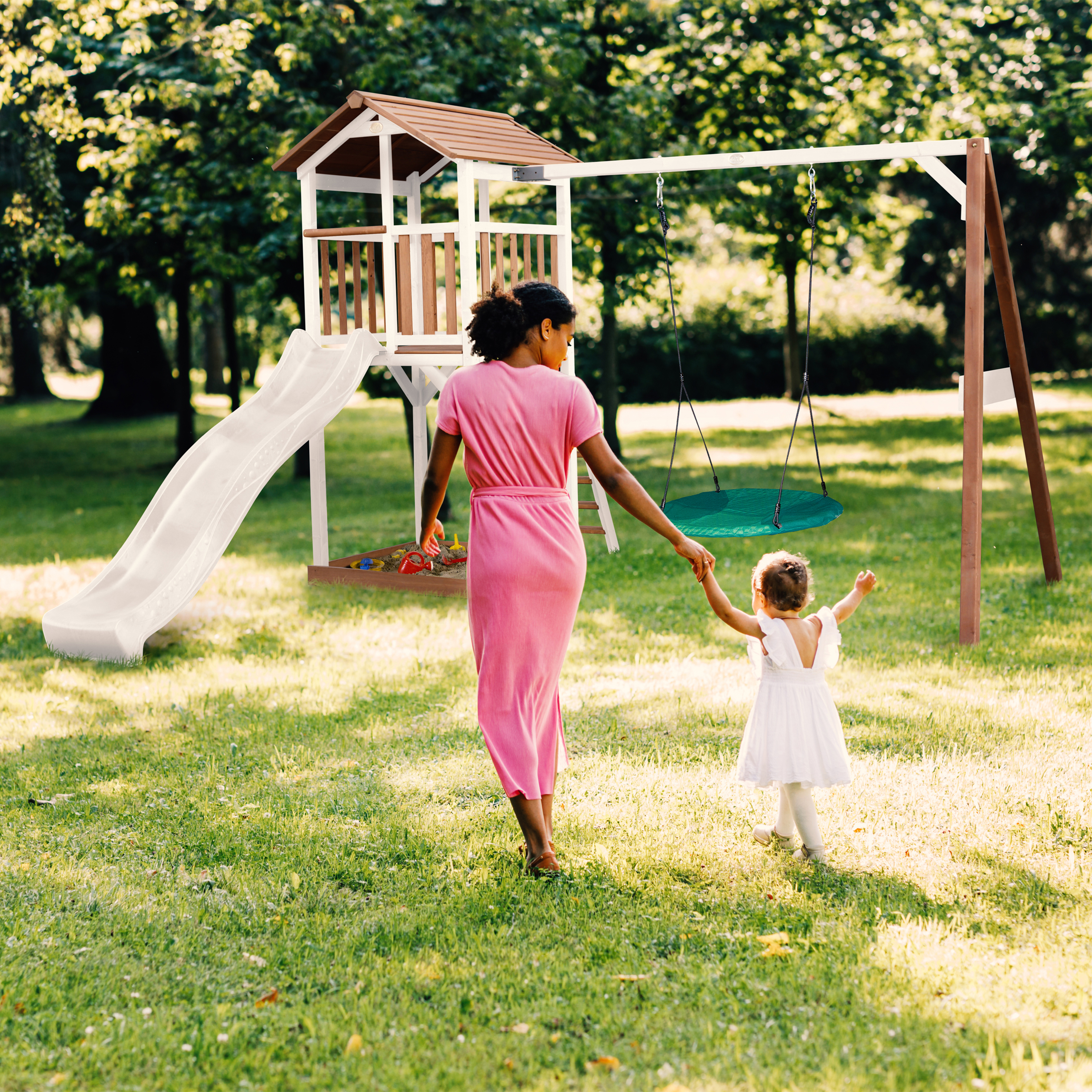 Frau und Kind gehen zu Spielturm mit Rutsche und Schaukel im Garten.