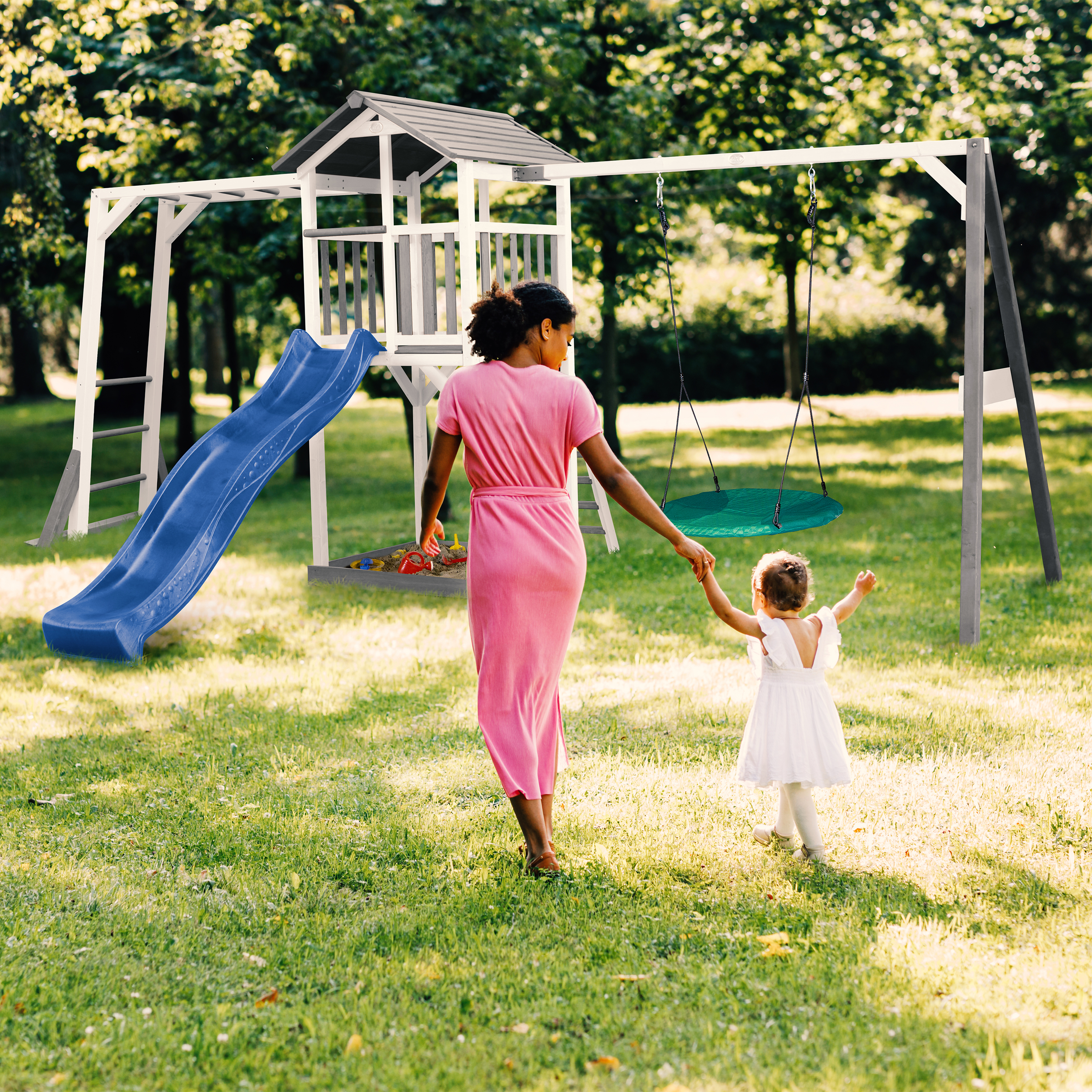 Mutter und Kind gehen zum Spielturm mit Rutsche und Schaukel im Garten.