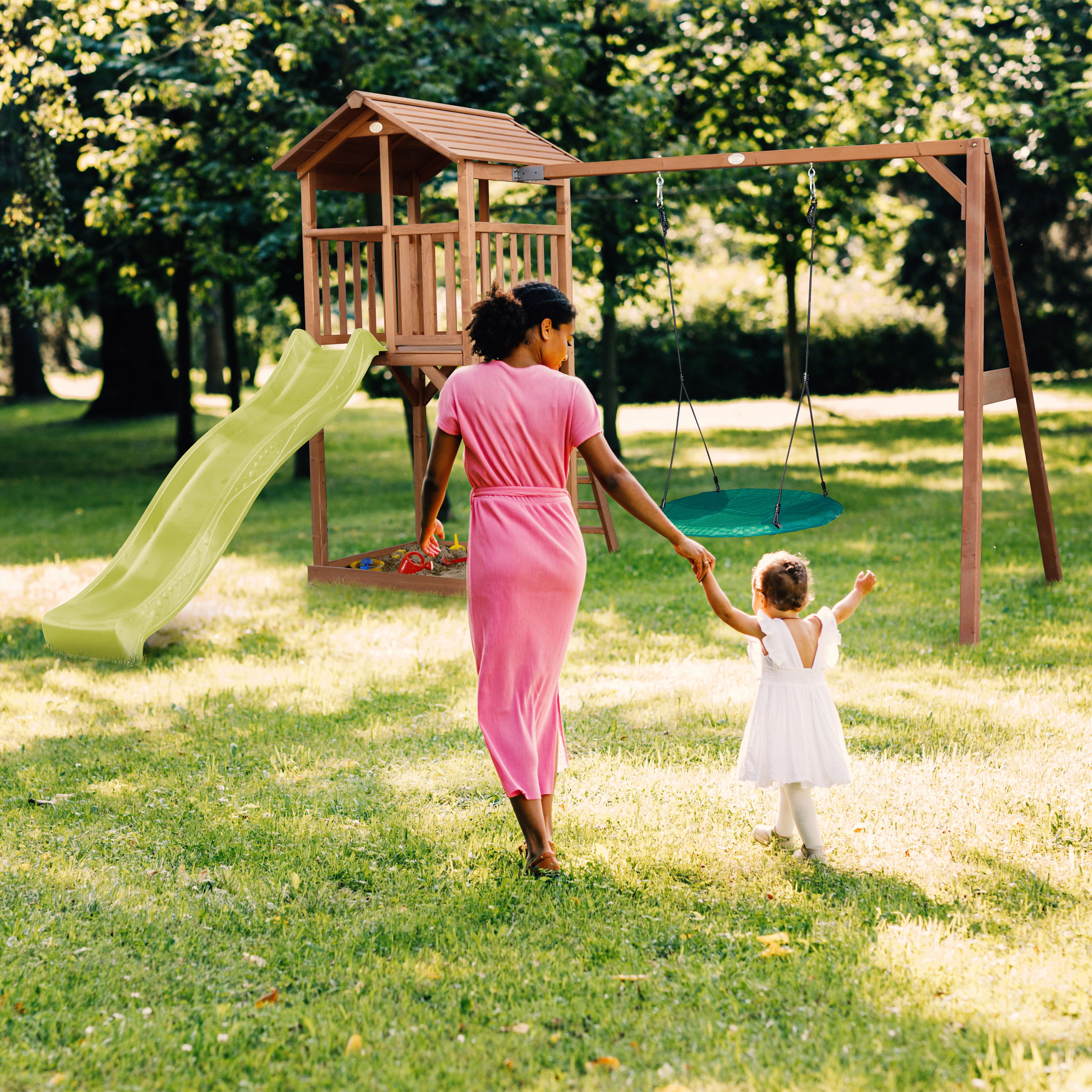 Mutter und Kind gehen zum Spielturm mit Rutsche und Schaukel im Garten.