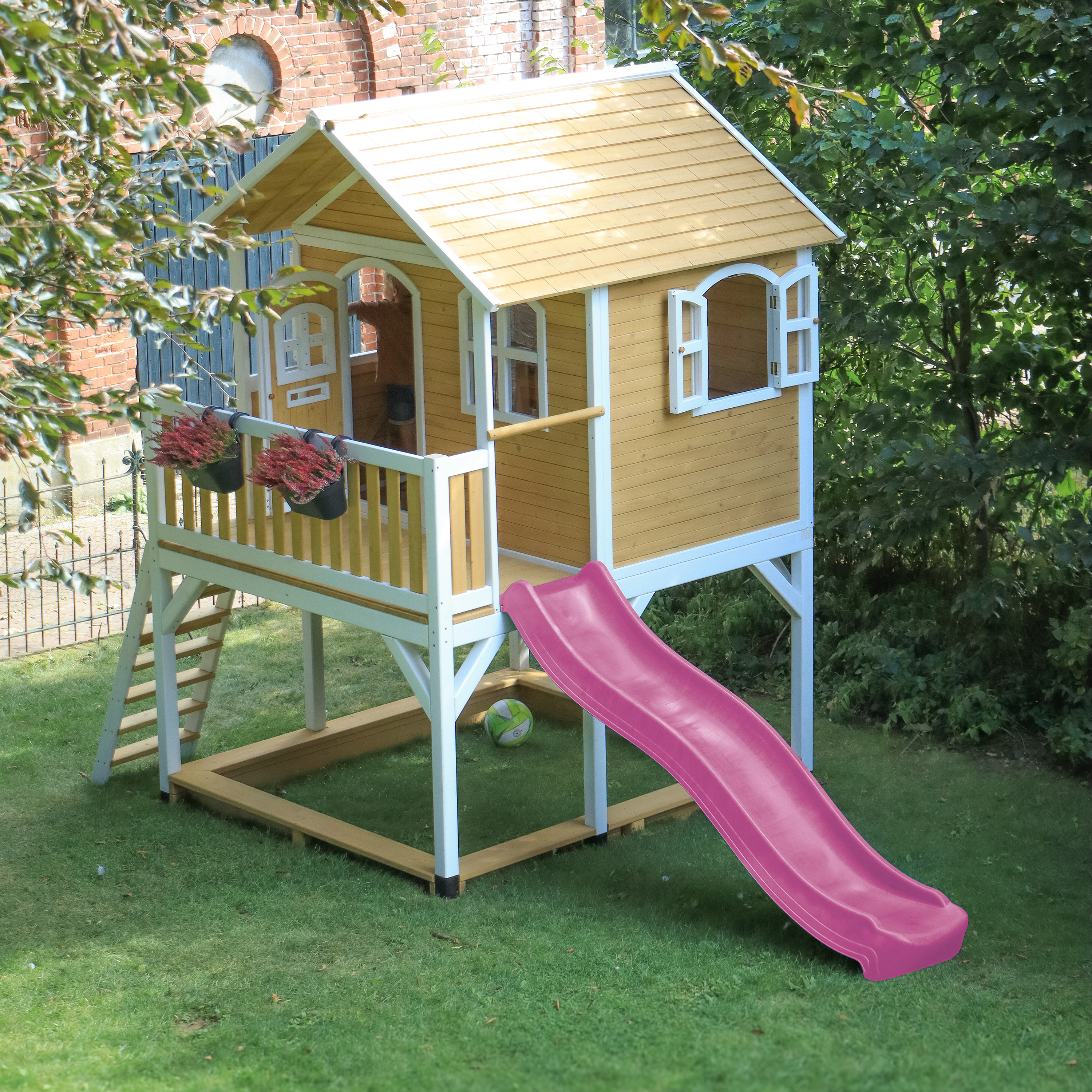 Ein gelbes Spielhaus mit Rutsche, Leiter und Sandkasten im Garten.