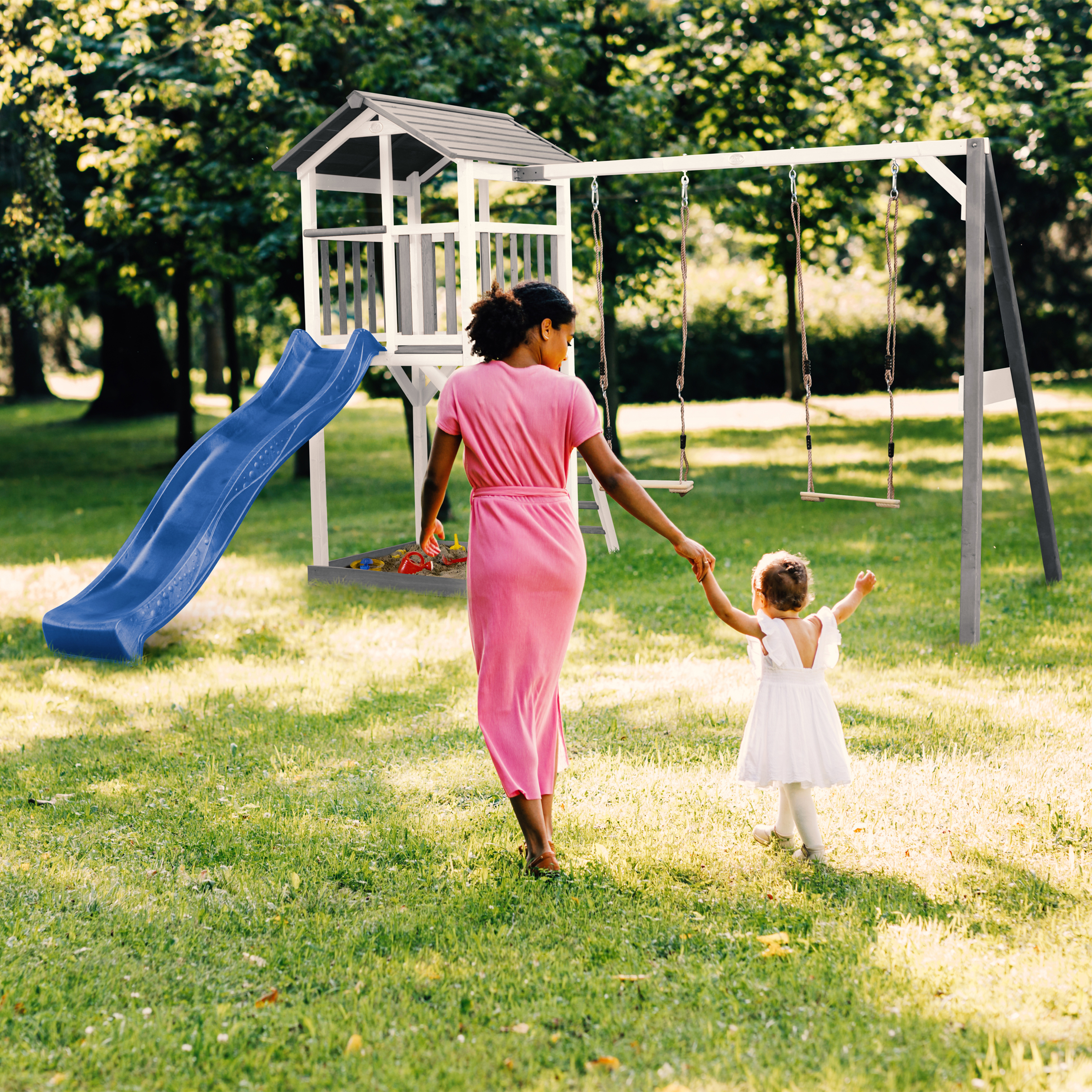 Frau und Kind gehen auf einem Spielplatz mit Rutsche und Schaukeln.