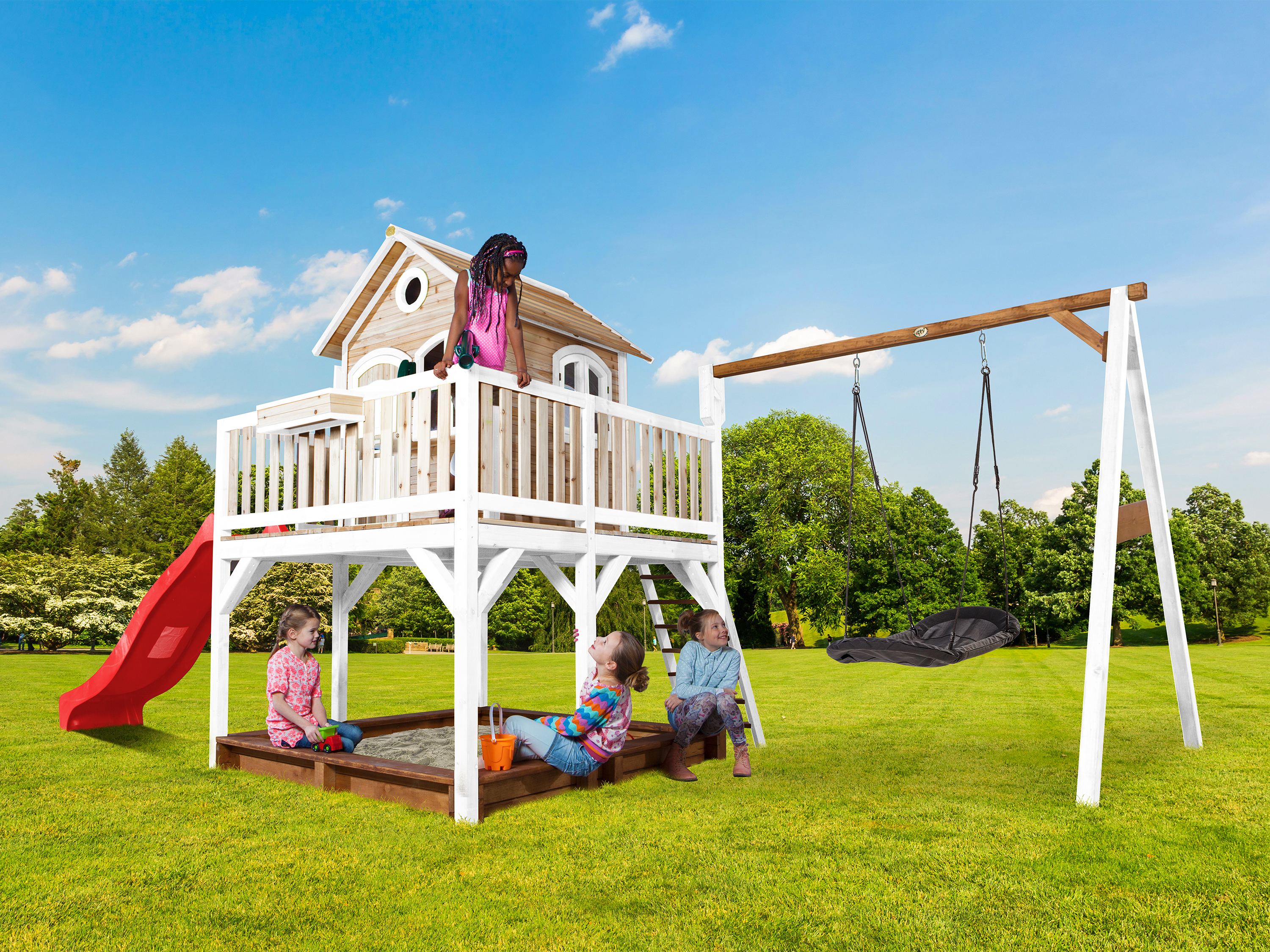 Kinder spielen auf einem Spielplatz mit Sandkasten, Rutsche und Schaukel.