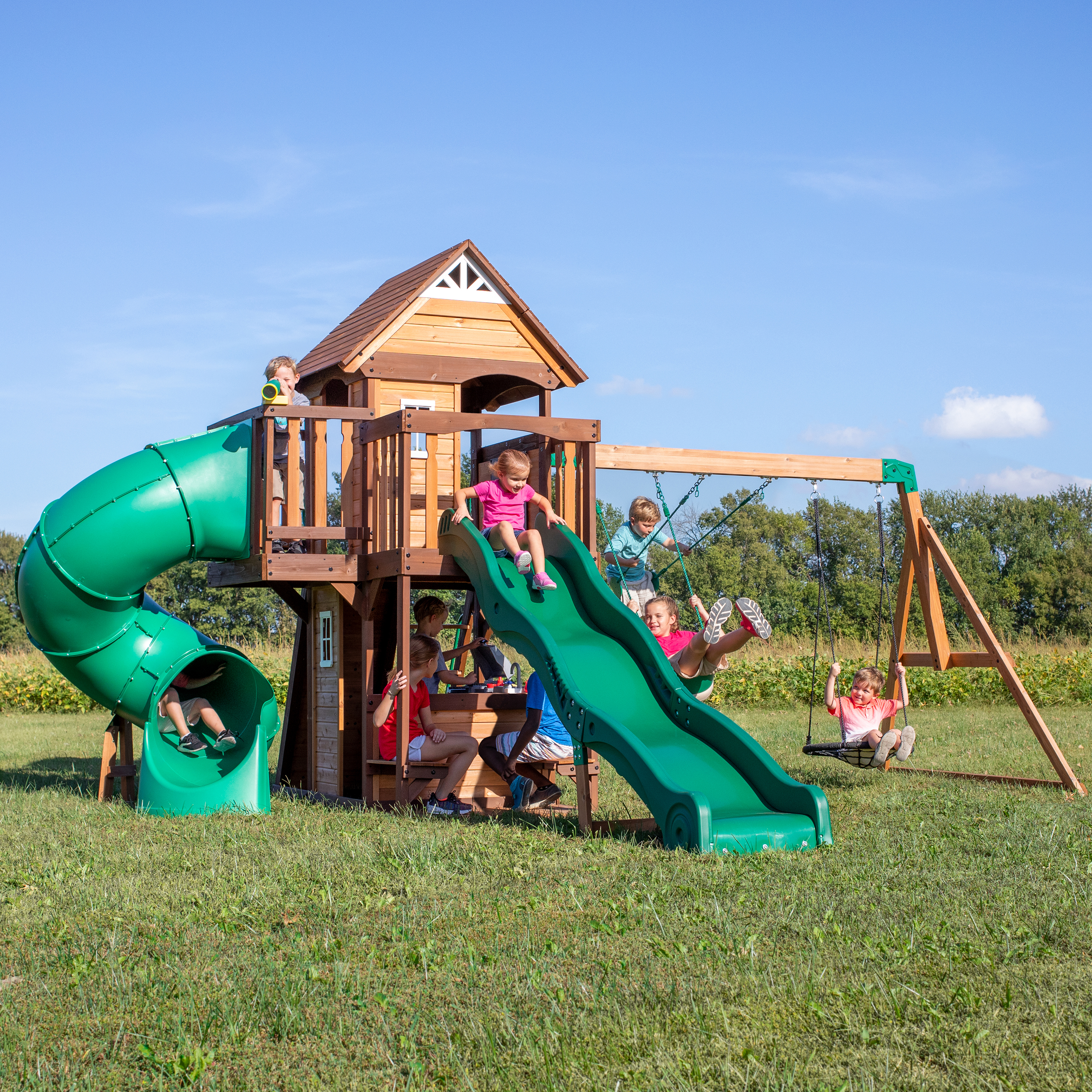 Kinder spielen auf einem Holzspielturm mit Rutschen und Schaukeln.