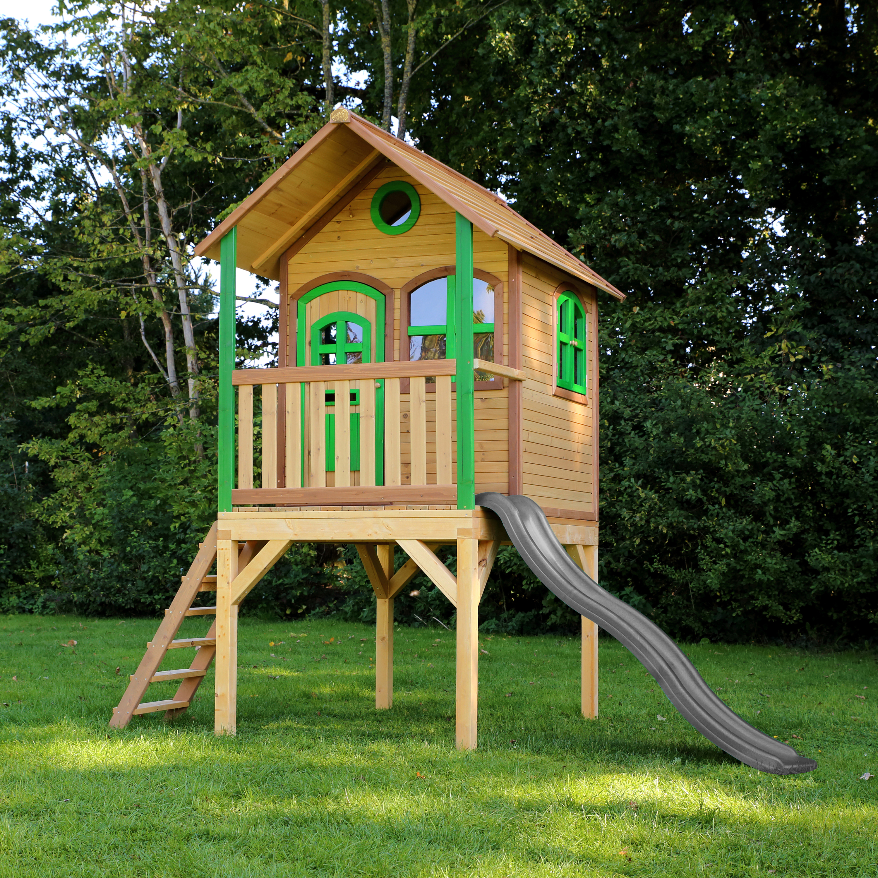 Ein hölzerner Spielturm mit Rutsche und Leiter auf grünem Rasen.
