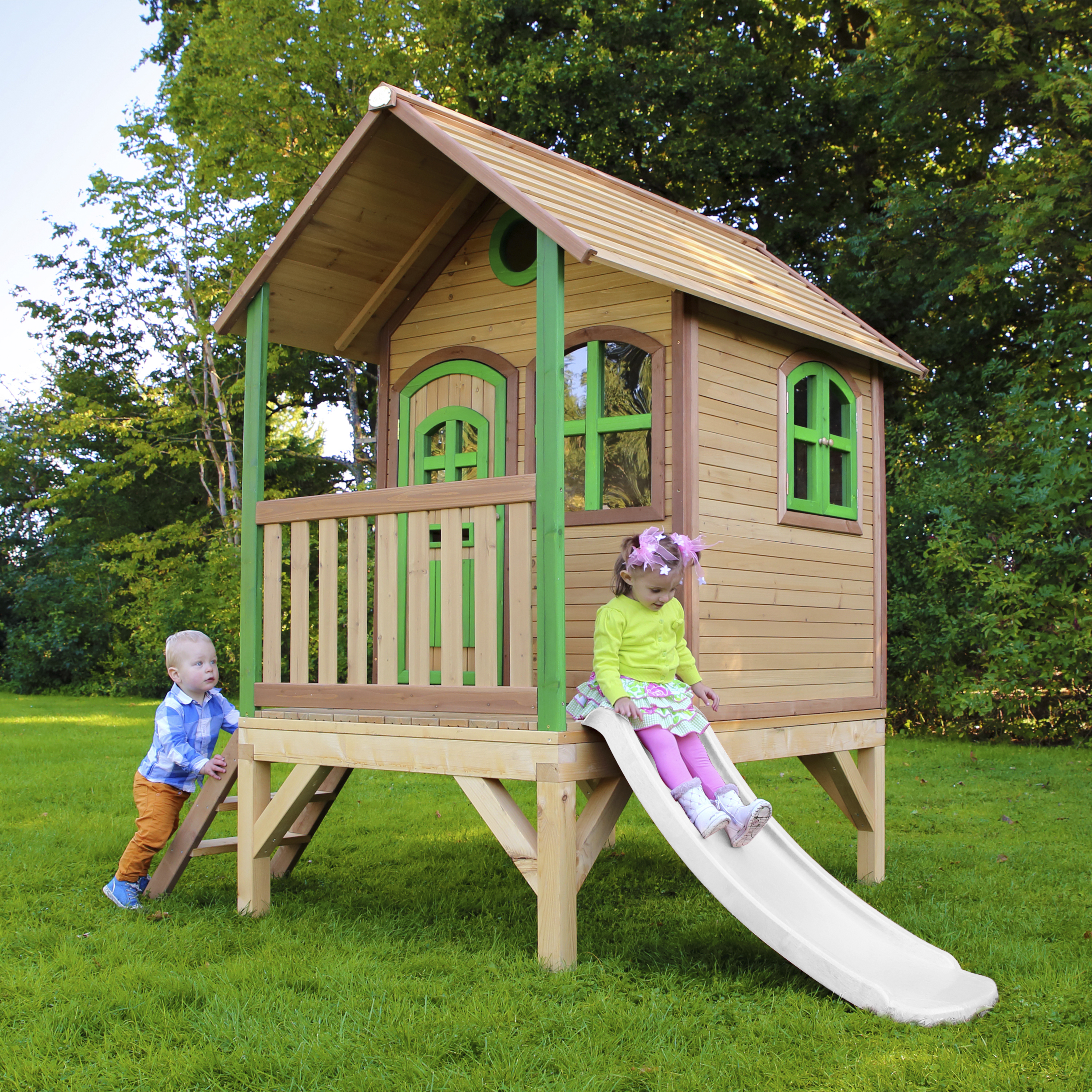 Zwei Kinder spielen auf einem Holzspielhaus mit Rutsche im Garten.