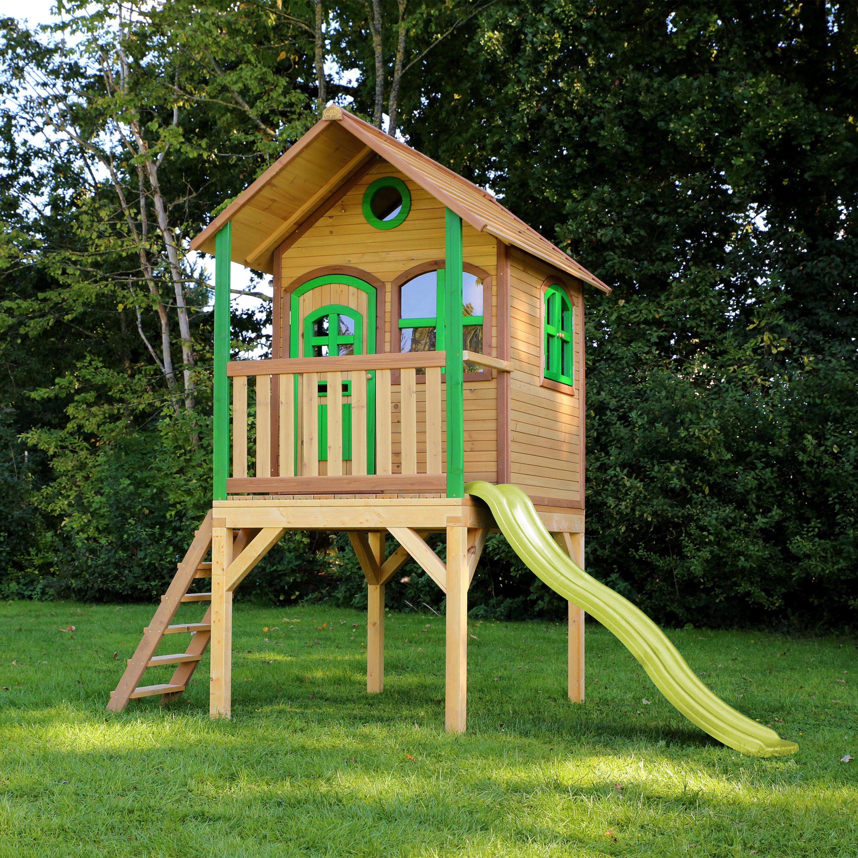 Ein Holzspielhaus mit grünen Fenstern und Rutsche auf Rasen.