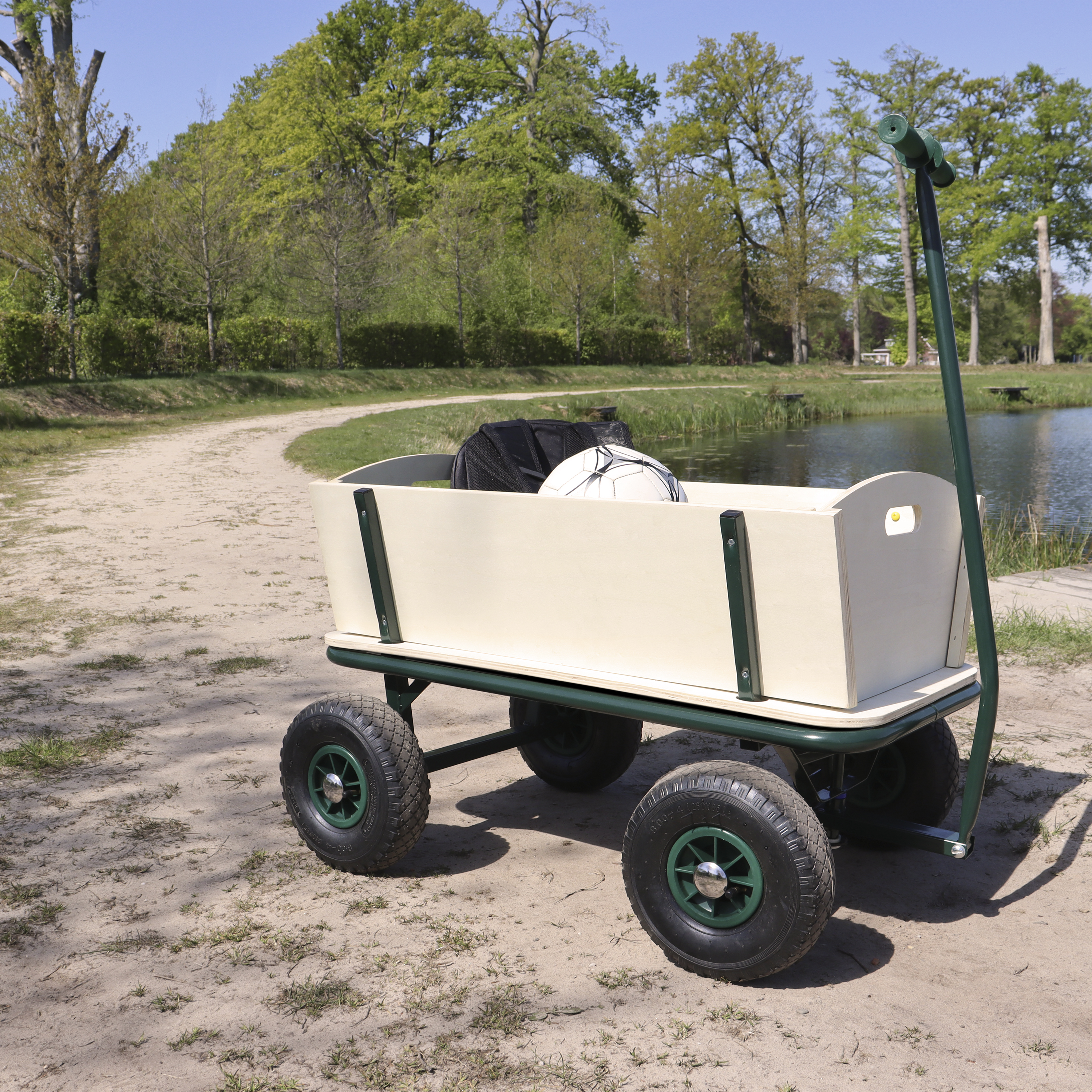 Ein beiger Bollerwagen mit grünen Rädern steht auf sandigem Boden.