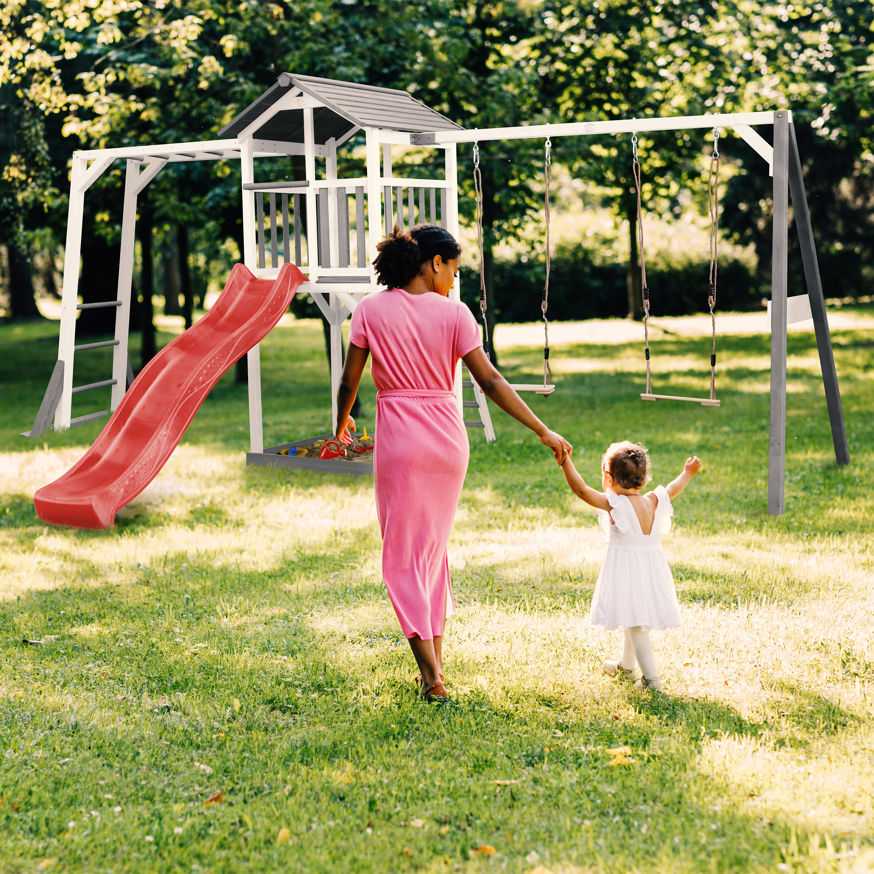 Frau und Kind gehen zu einem Spielgerüst mit Rutsche und Schaukeln im Garten.