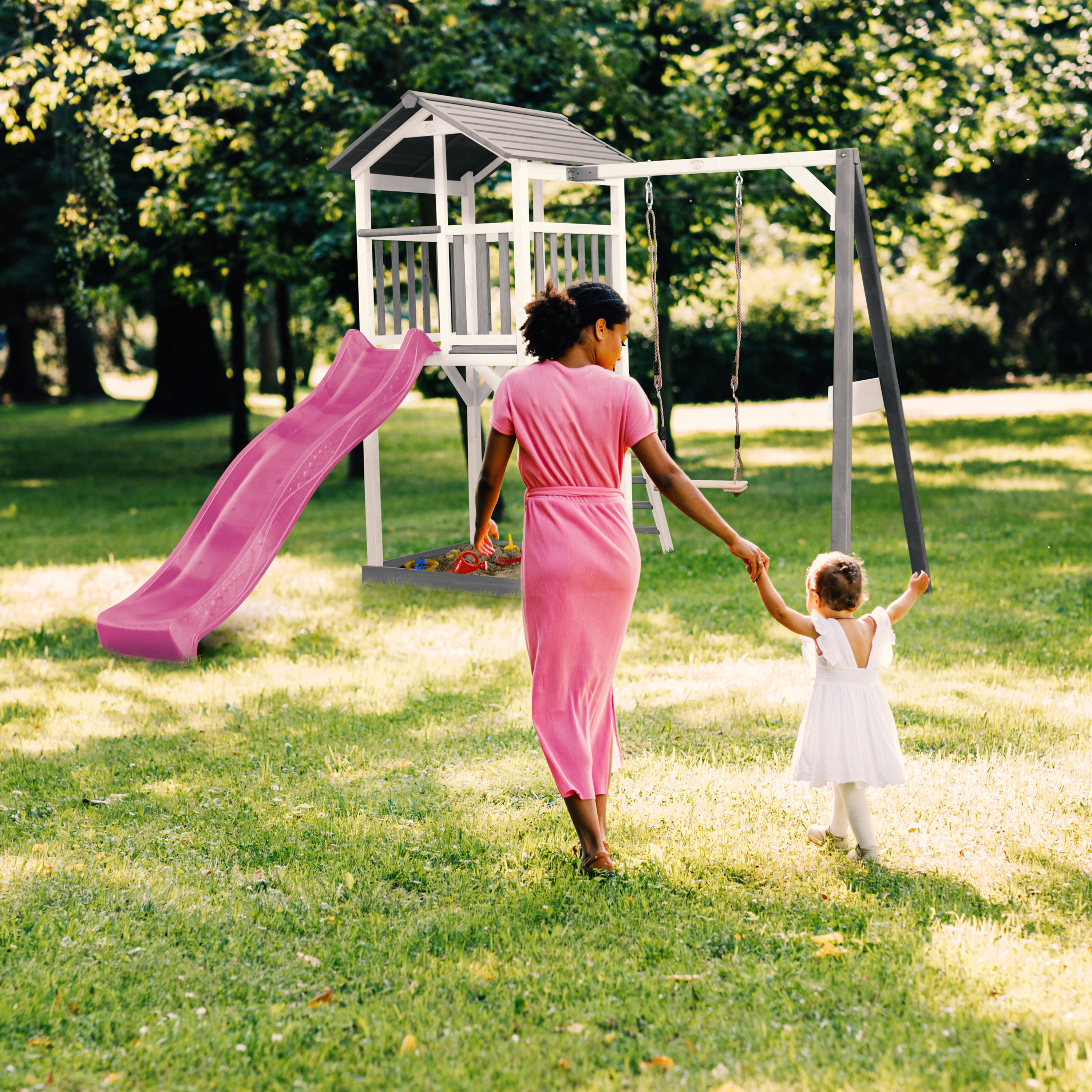 Eine Frau und ein Kind gehen auf einem Spielplatz mit Rutsche und Schaukel.