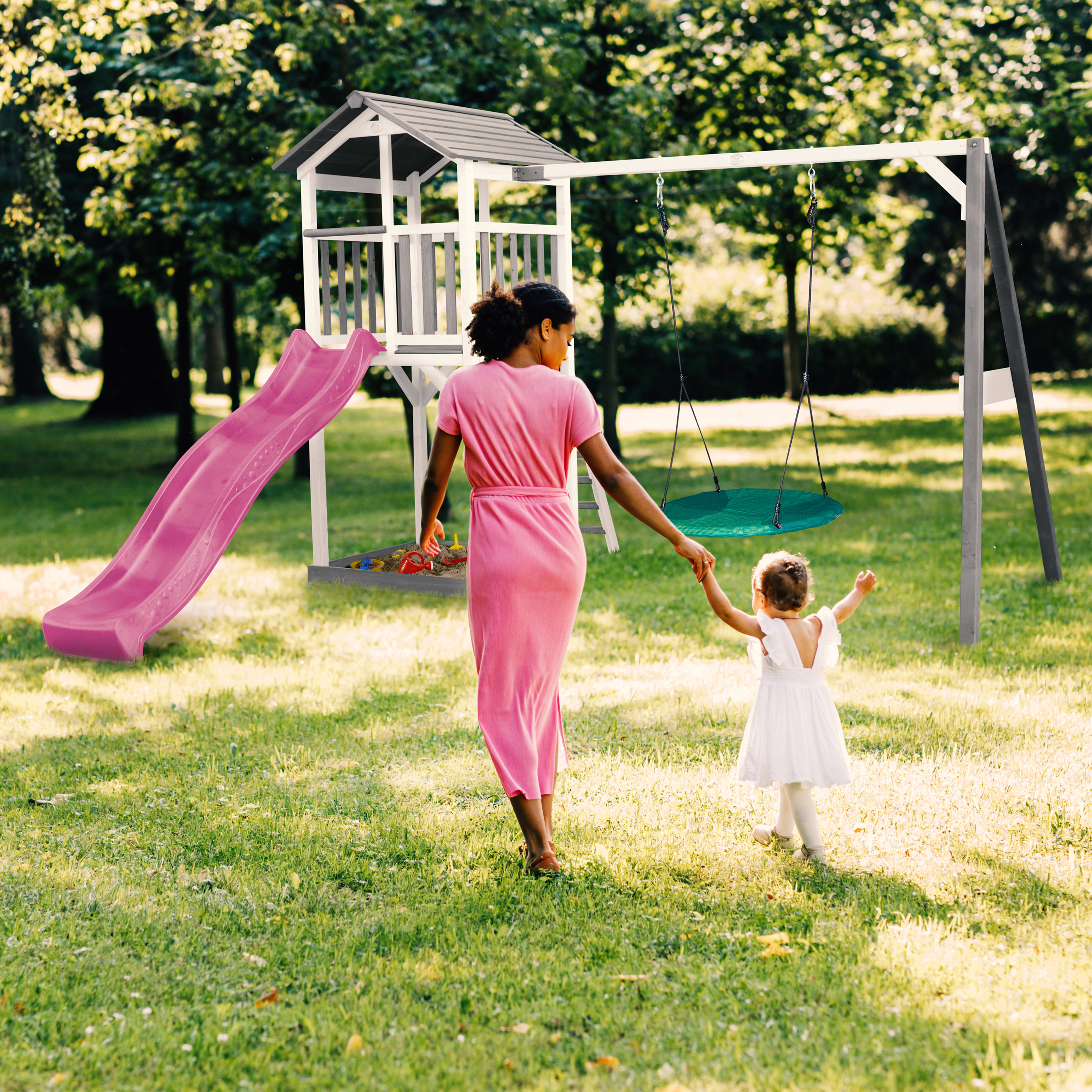 Mutter und Kind gehen auf einem Spielplatz mit Rutsche und Schaukel im Gras.