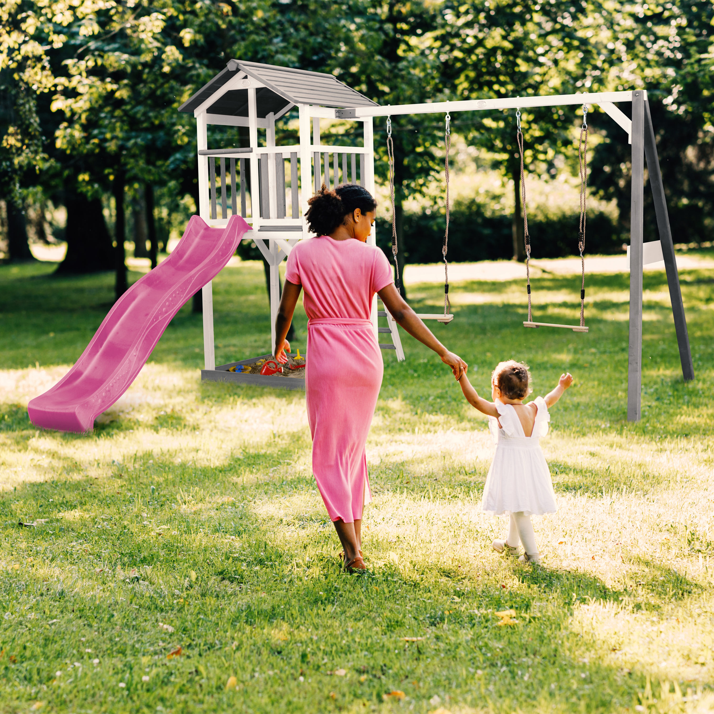 Frau mit Kind auf einem Spielplatz mit Rutsche und Schaukel im Gras.