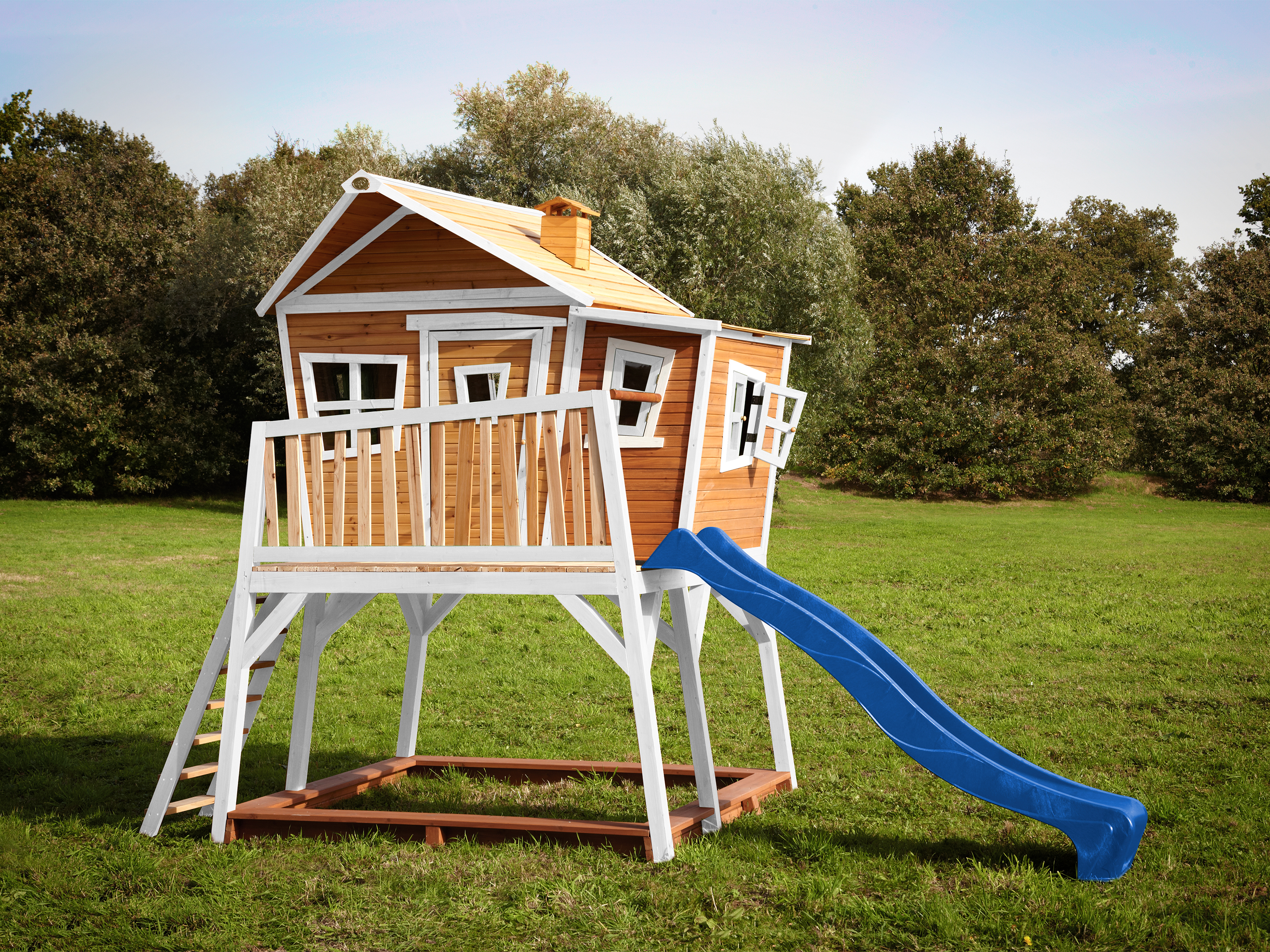 Ein Holzspielhaus mit Rutsche auf einer grünen Wiese.