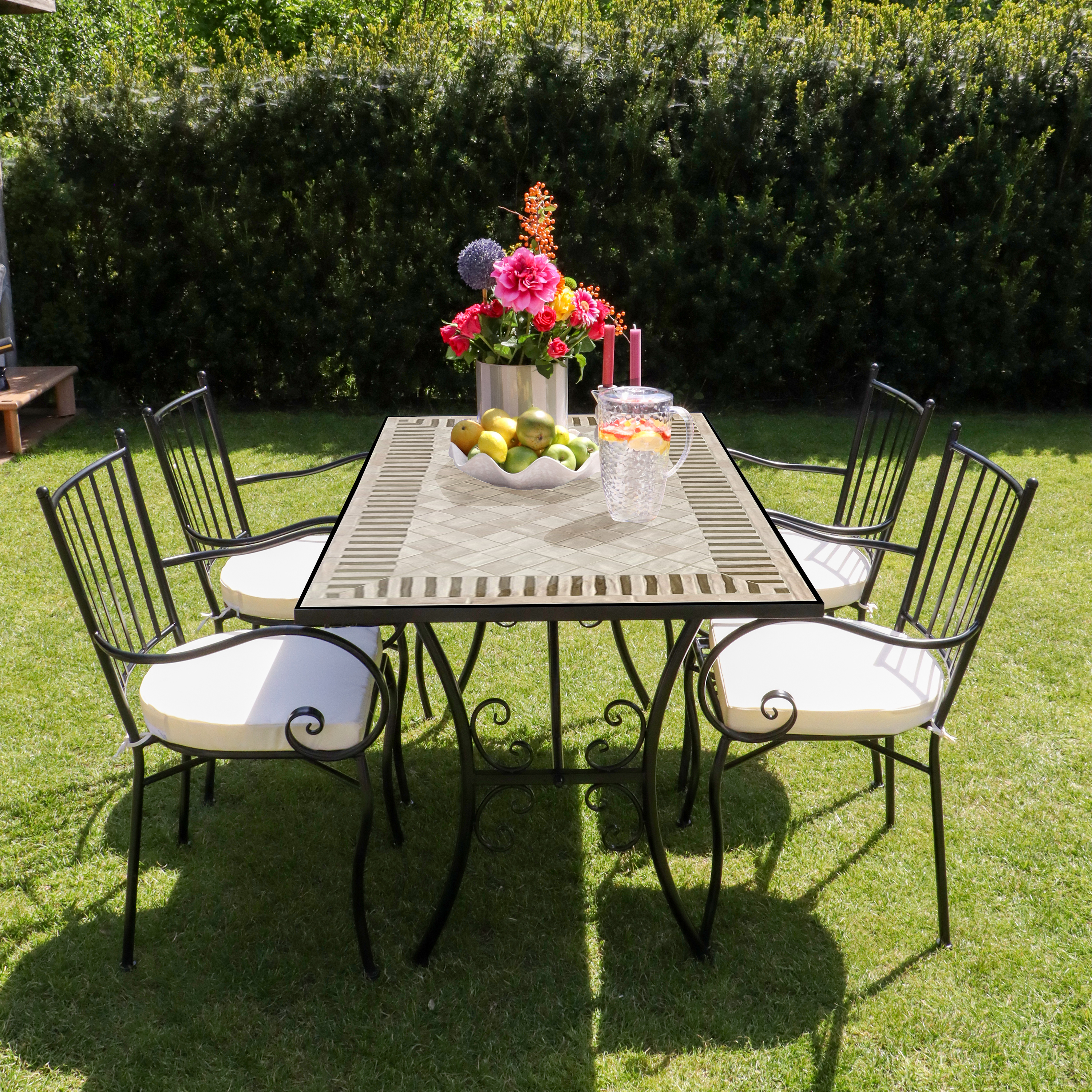 Ein Gartentisch mit vier Stühlen, dekoriert mit Blumen, Obst und Getränken.