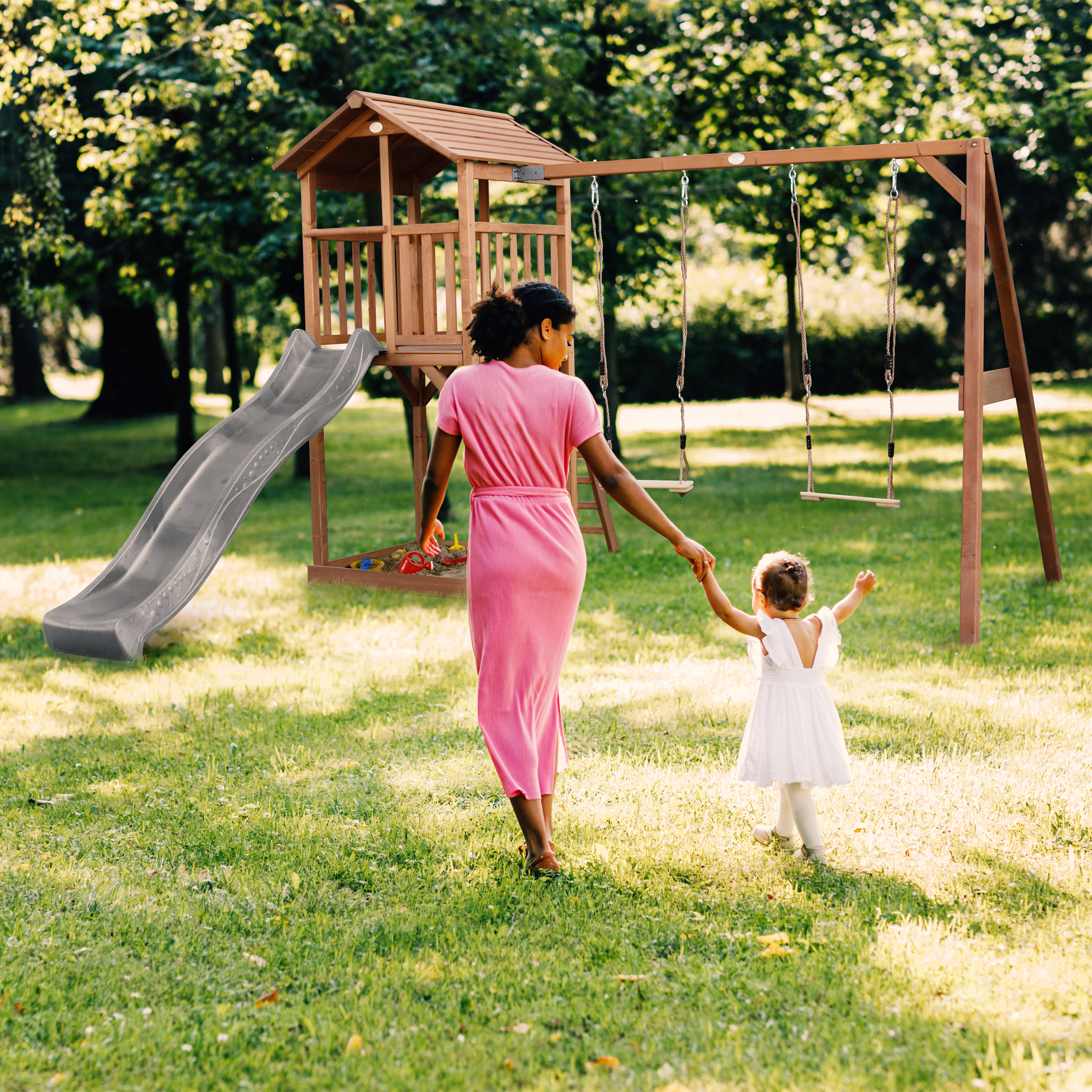 Frau und Kind gehen zum Spielplatz mit Rutsche und Schaukeln im Park.