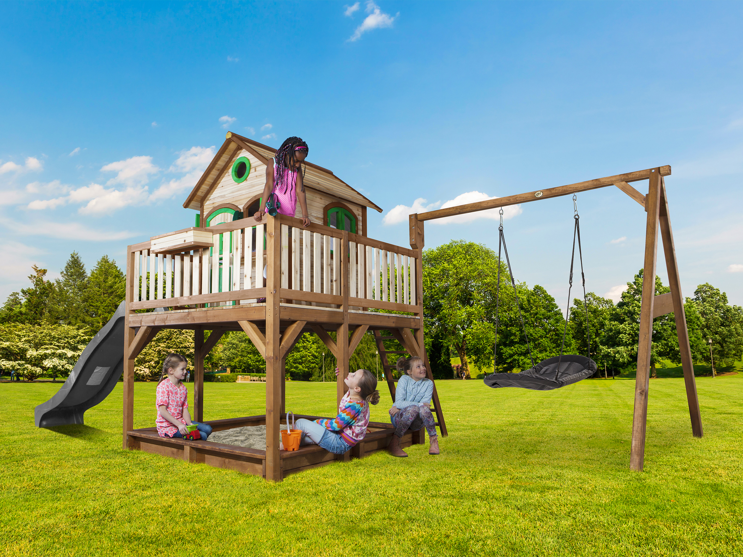 Kinder spielen auf einem Holzspielturm mit Rutsche und Schaukel an einem sonnigen Tag.