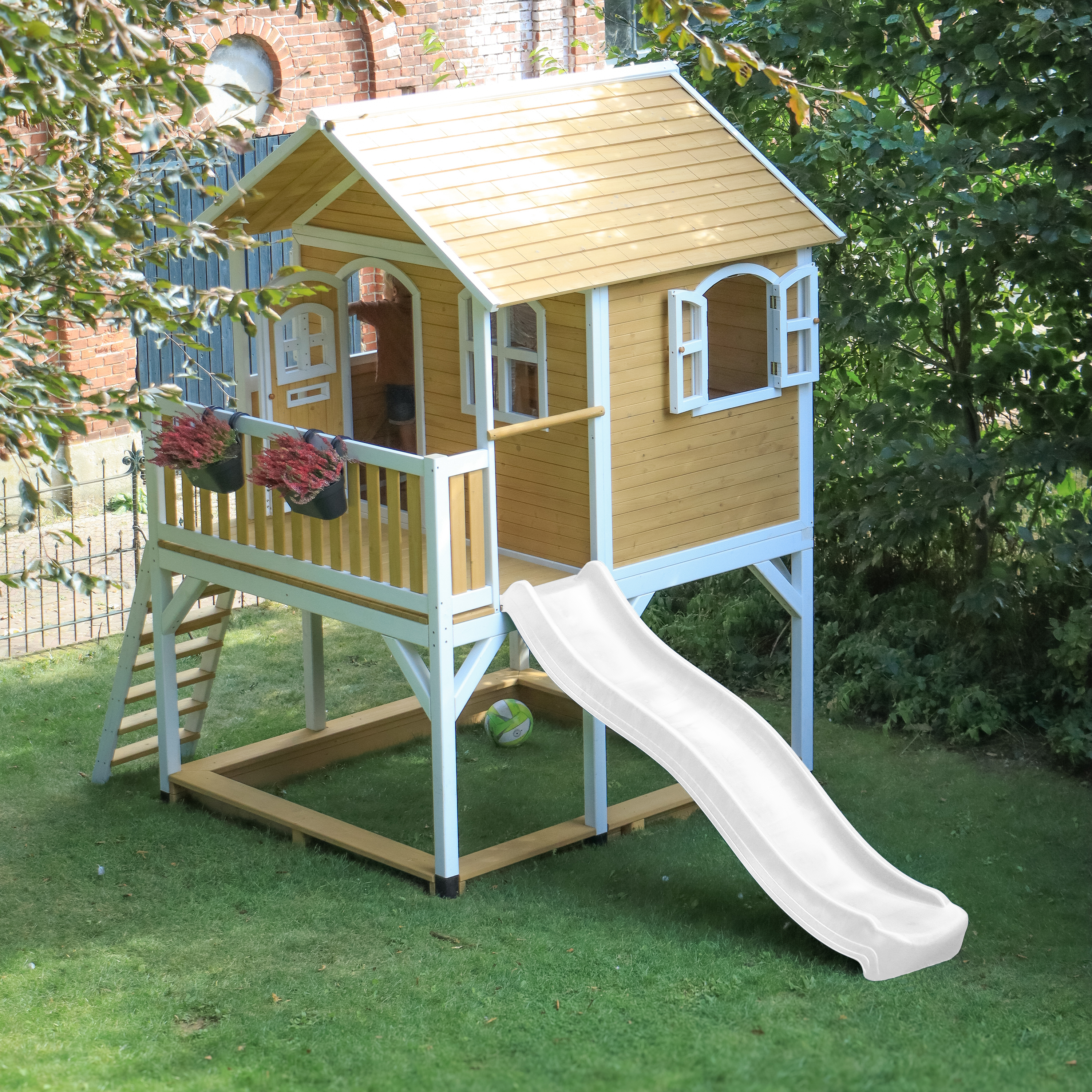Ein gelbes Spielhaus mit Rutsche und Kletterleiter auf grünem Gras.