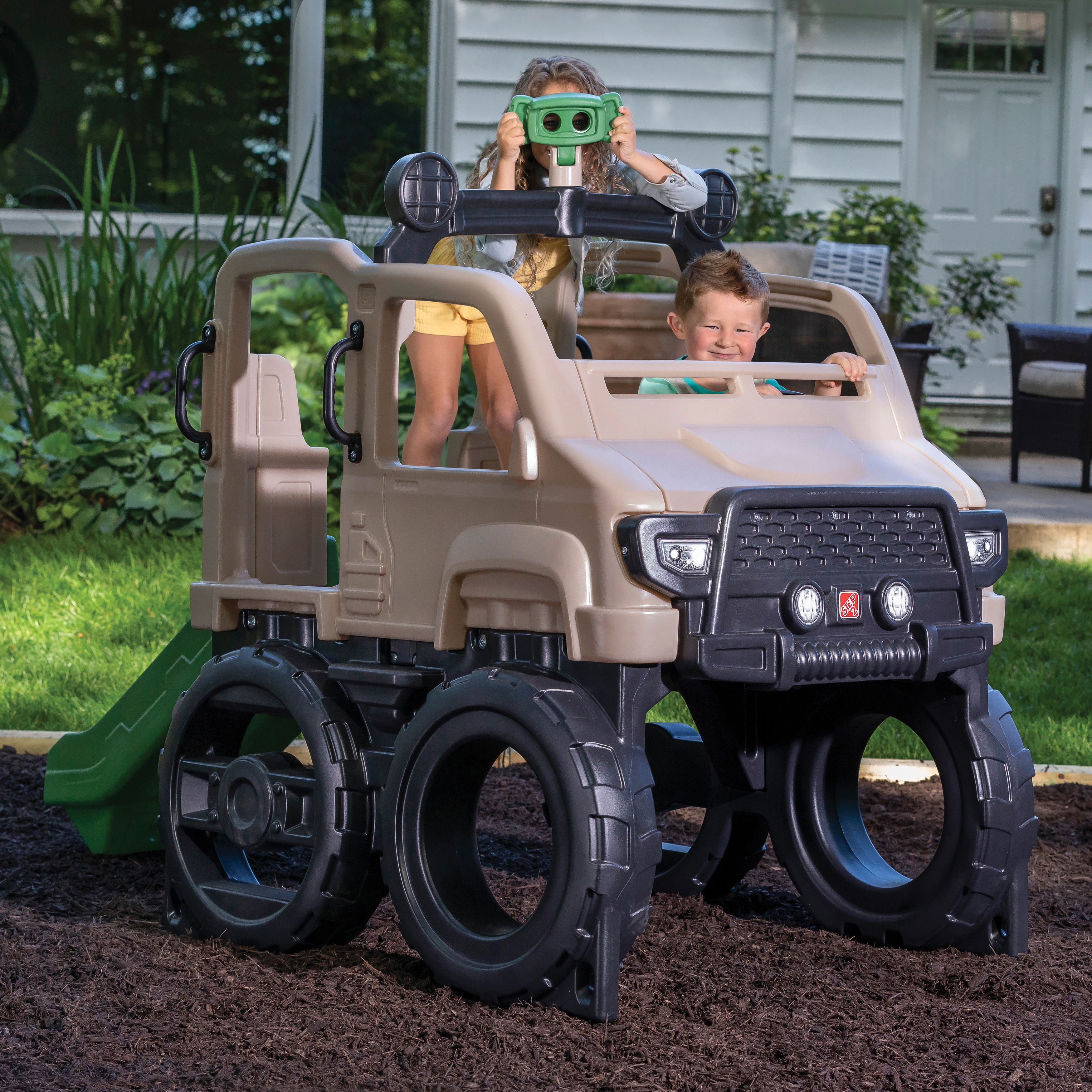 Kinder spielen in einem großen, beigefarbenen Spielzeug-Jeep mit Rutsche.
