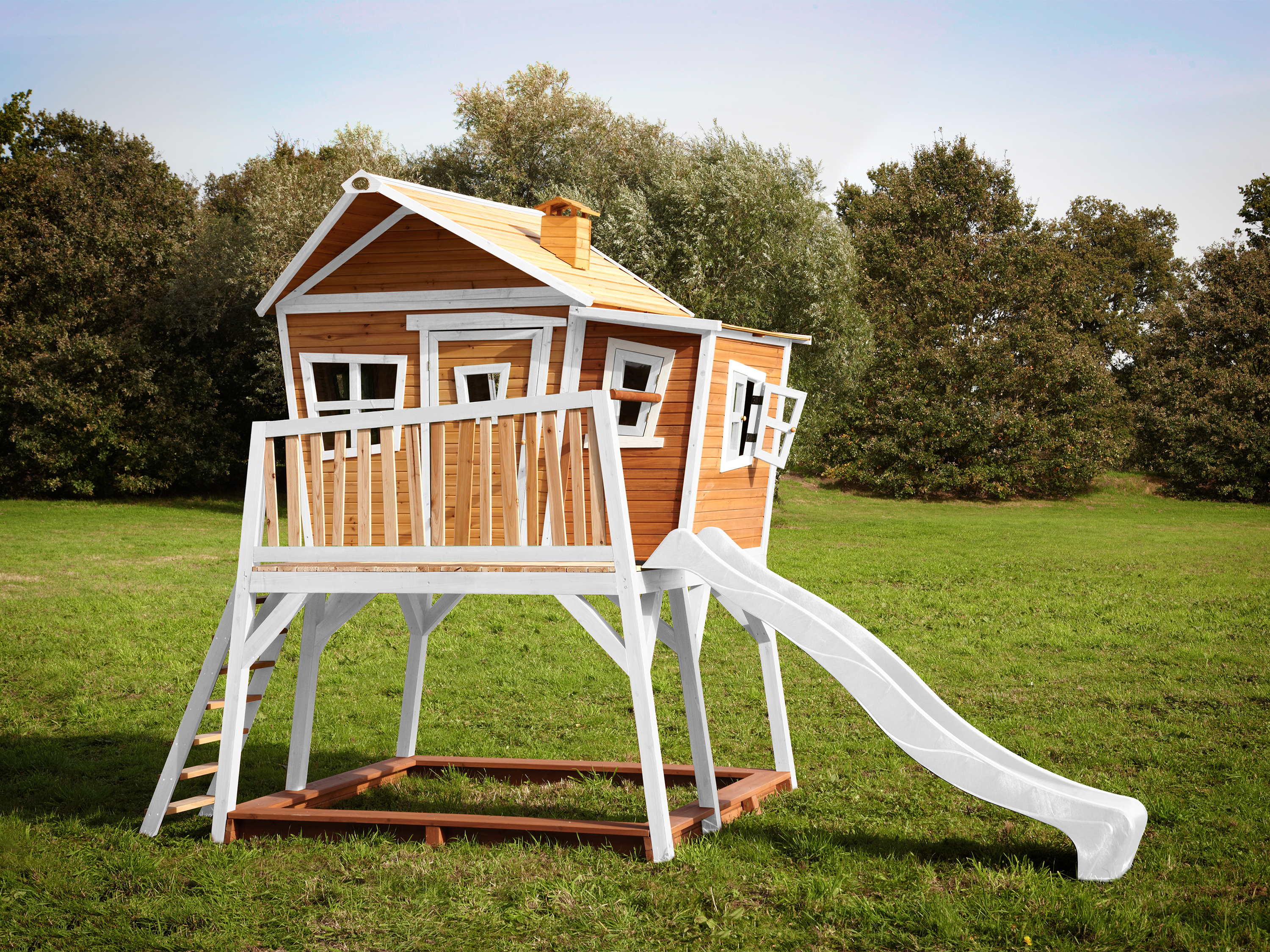 Holz-Spielhaus mit Rutsche und Leiter auf einer grünen Wiese.