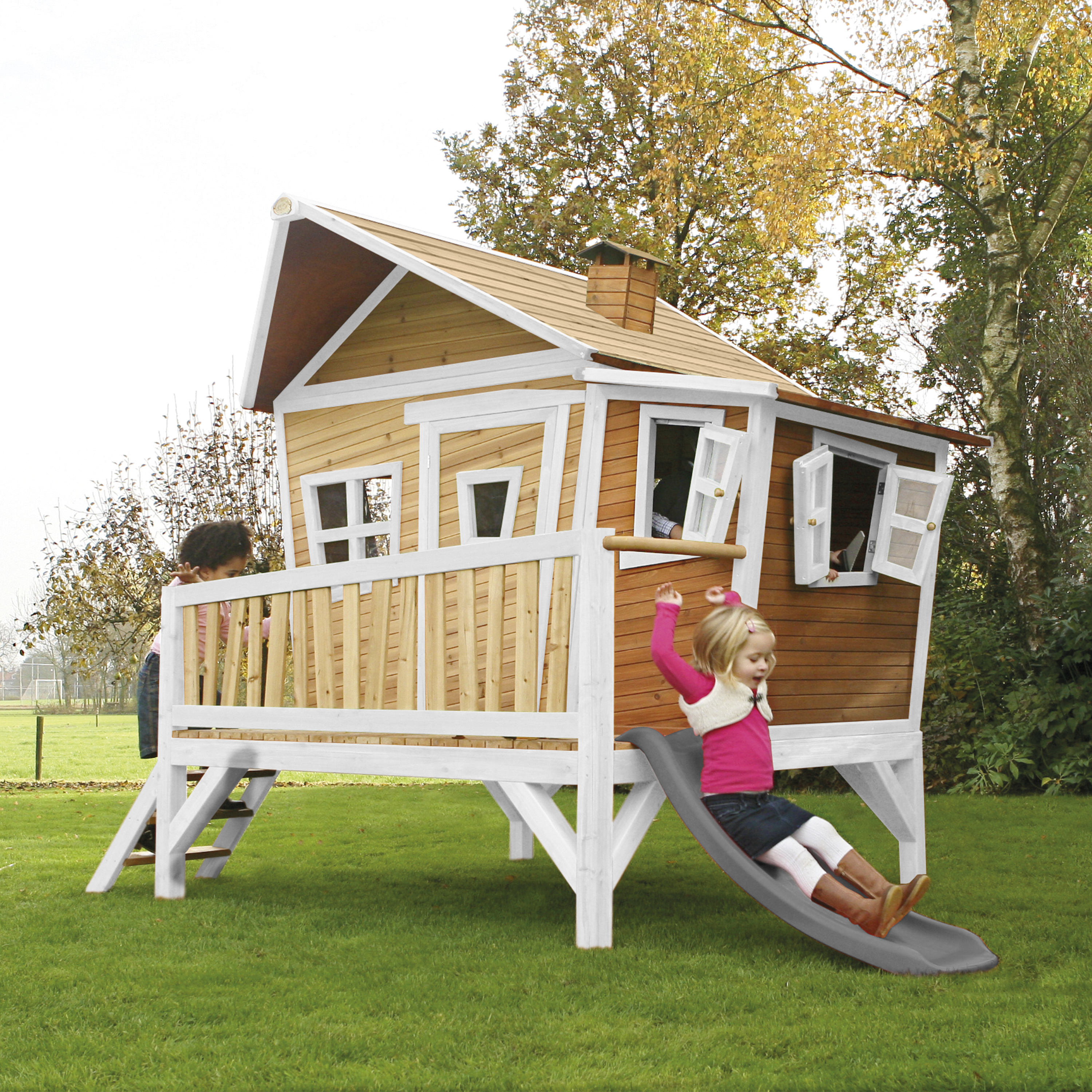 Kinder spielen auf einem Holzspielhaus mit Rutsche im Garten.