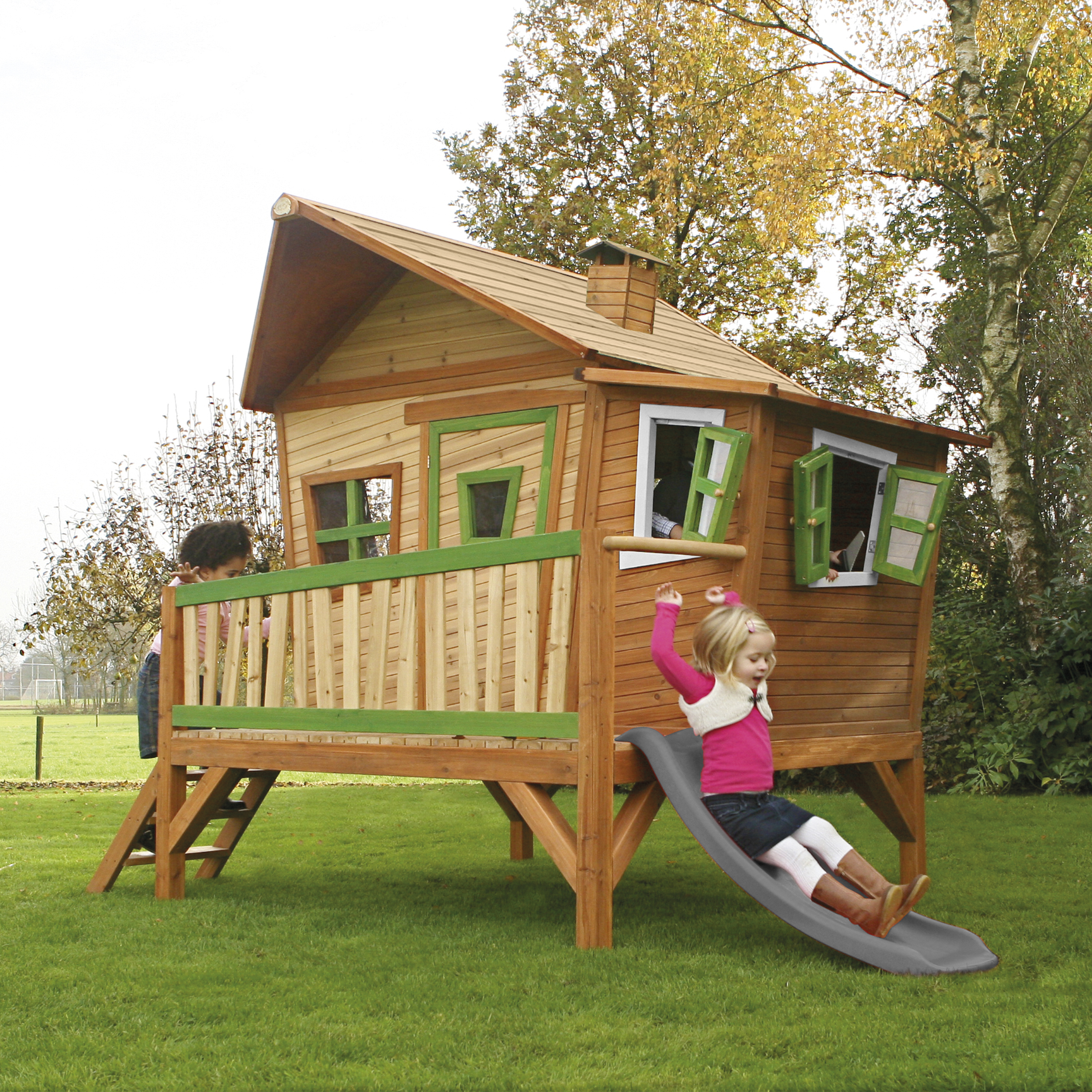 Zwei Kinder spielen auf einem Baumhaus mit Rutsche im Garten.