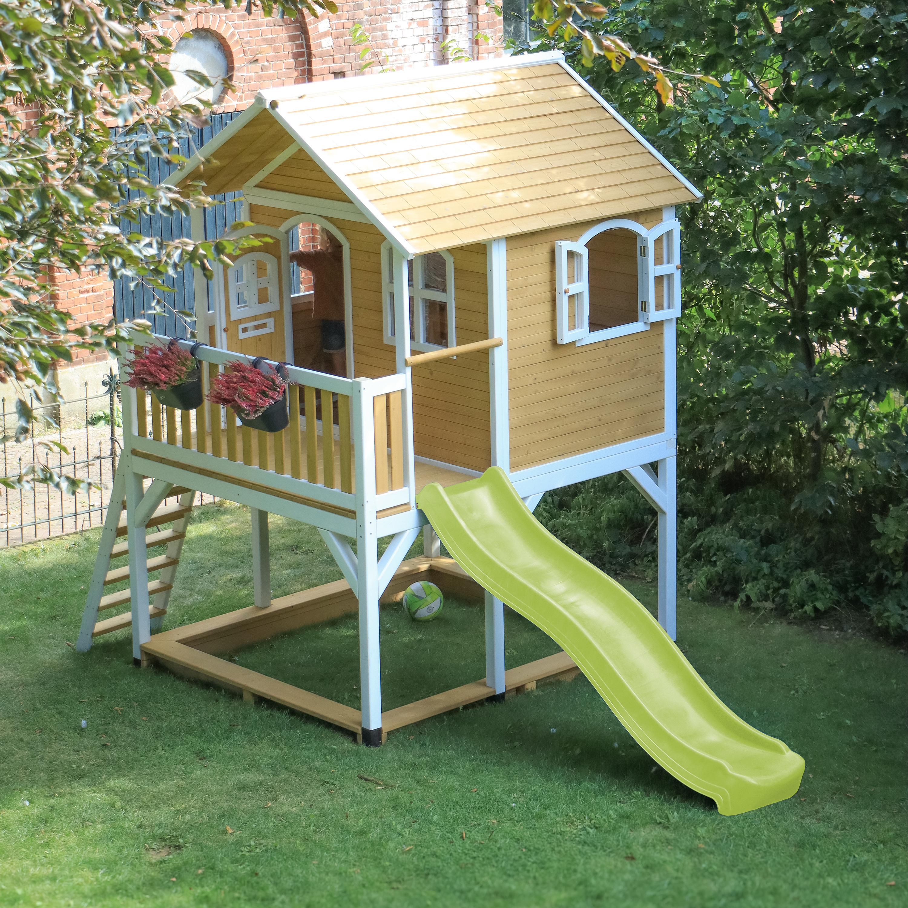 Ein gelbes Spielhaus mit Rutsche und Leiter im Garten.