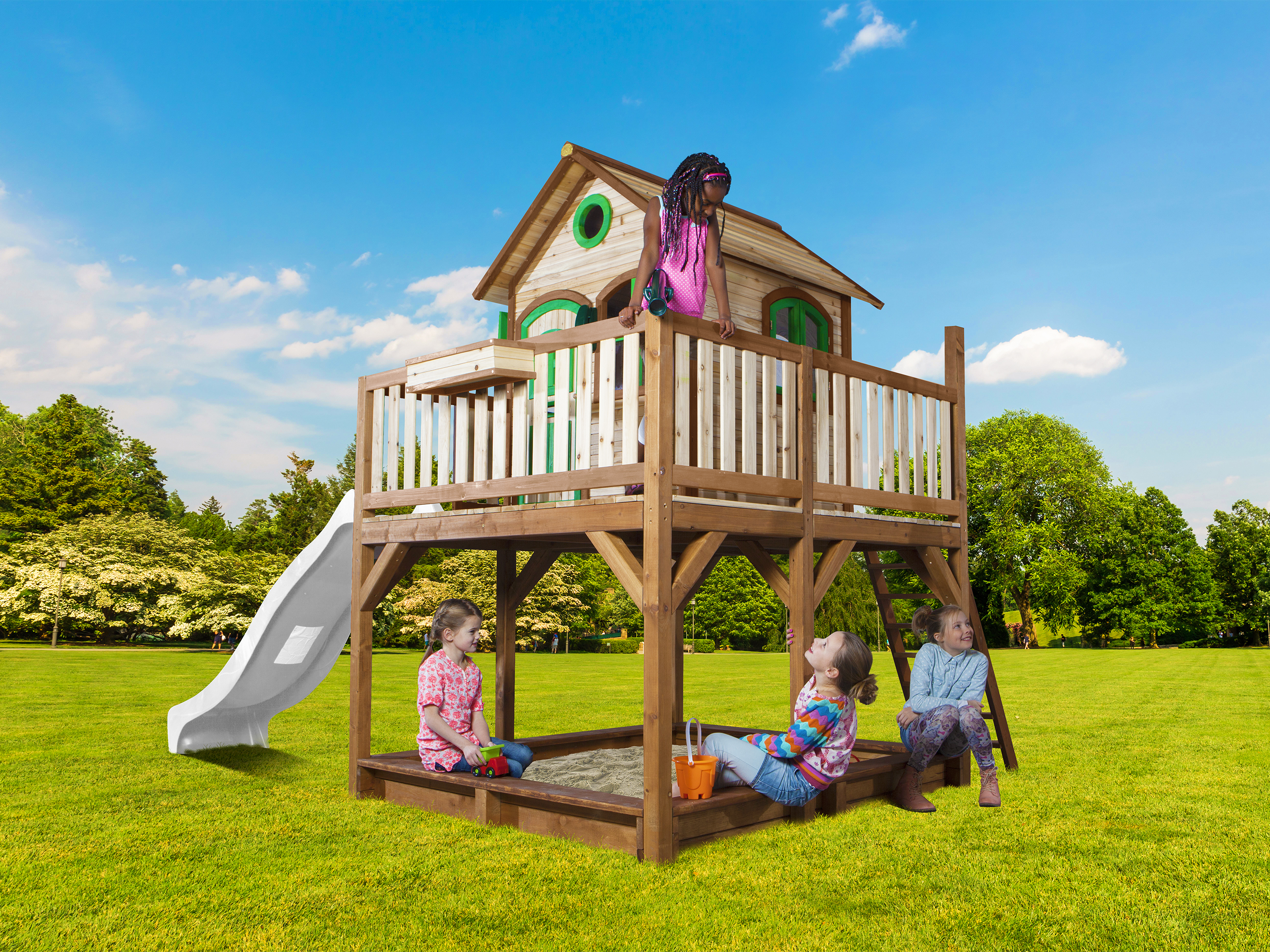 Kinder spielen auf einem Holzspielhaus mit Rutsche und Sandkasten im Garten.