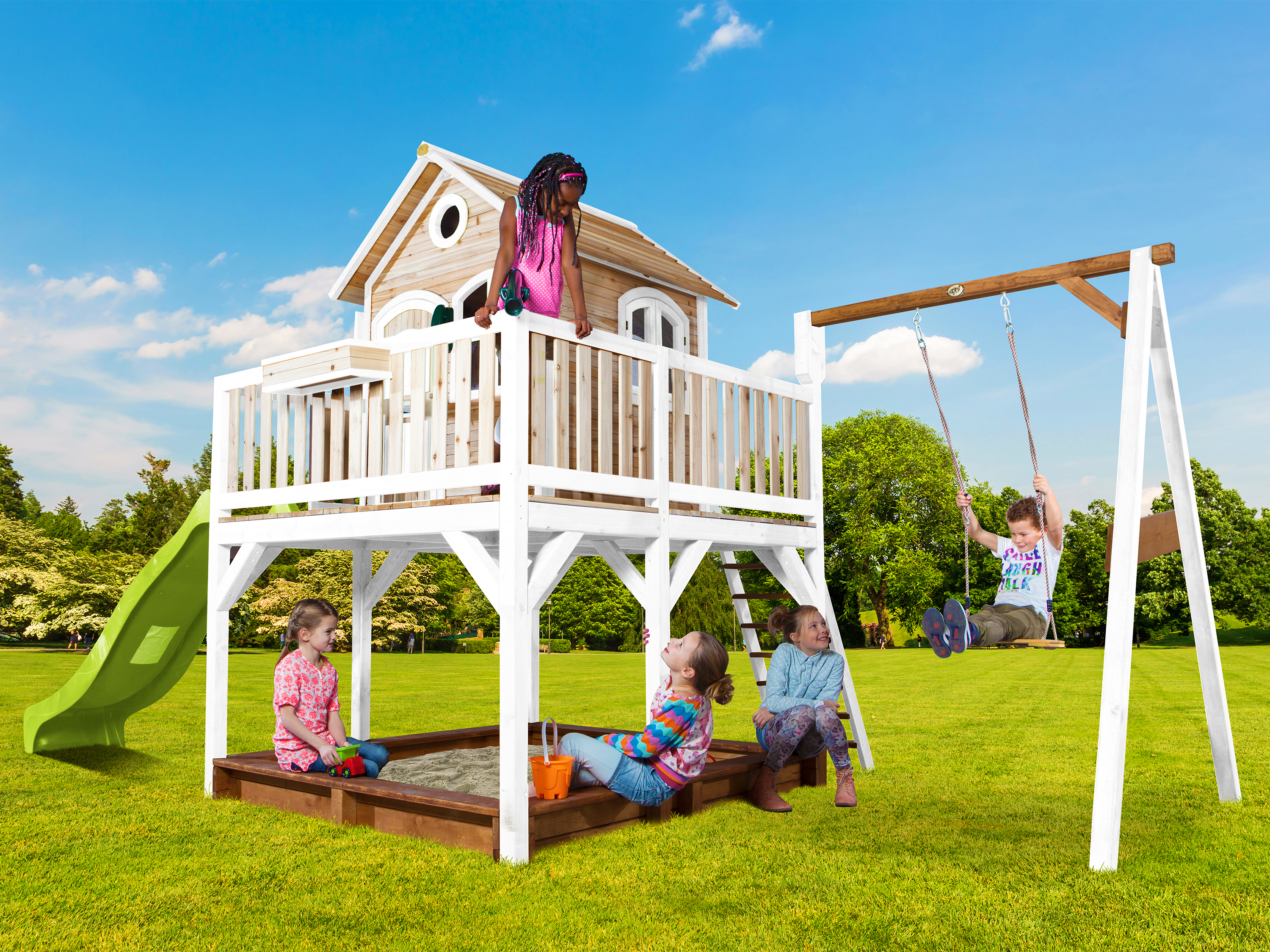 Kinder spielen auf einem Spielplatz mit einem Baumhaus, einer Rutsche und einer Schaukel.