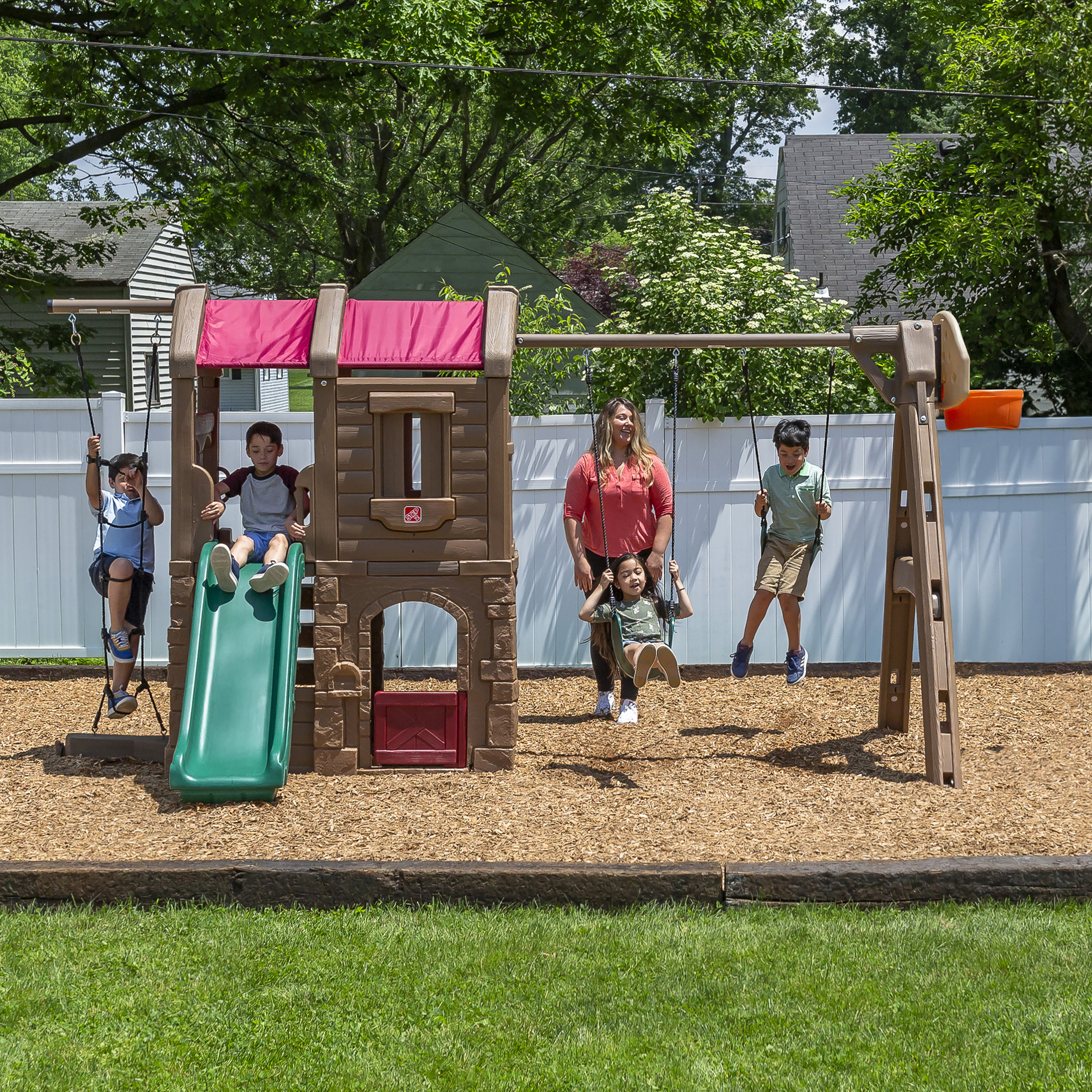 Kinder spielen auf einem Spielplatz mit Rutsche und Schaukeln unter Bäumen.