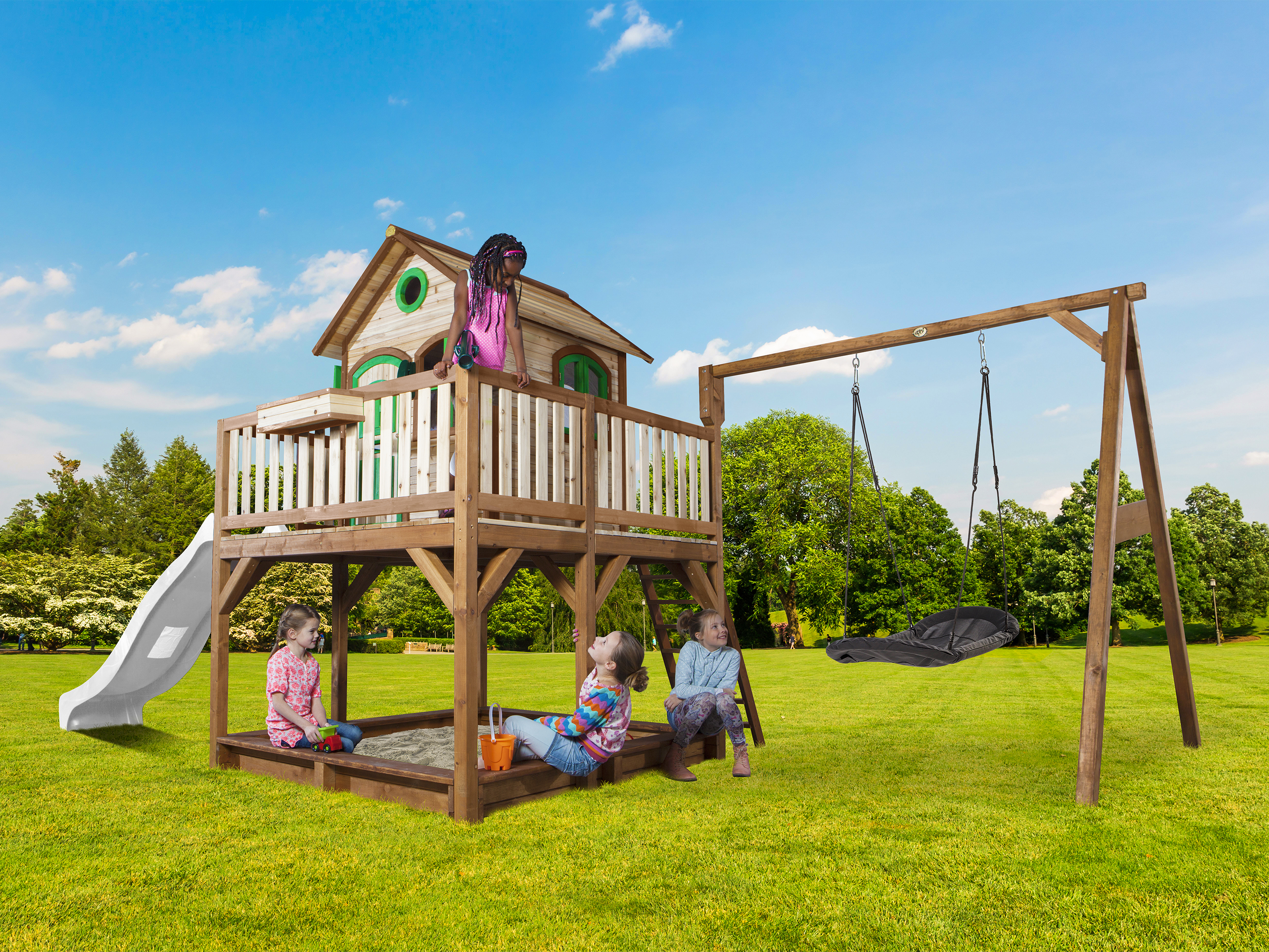 Kinder spielen auf einem Spielplatz mit Rutsche, Schaukel und Sandkasten an einem sonnigen Tag.