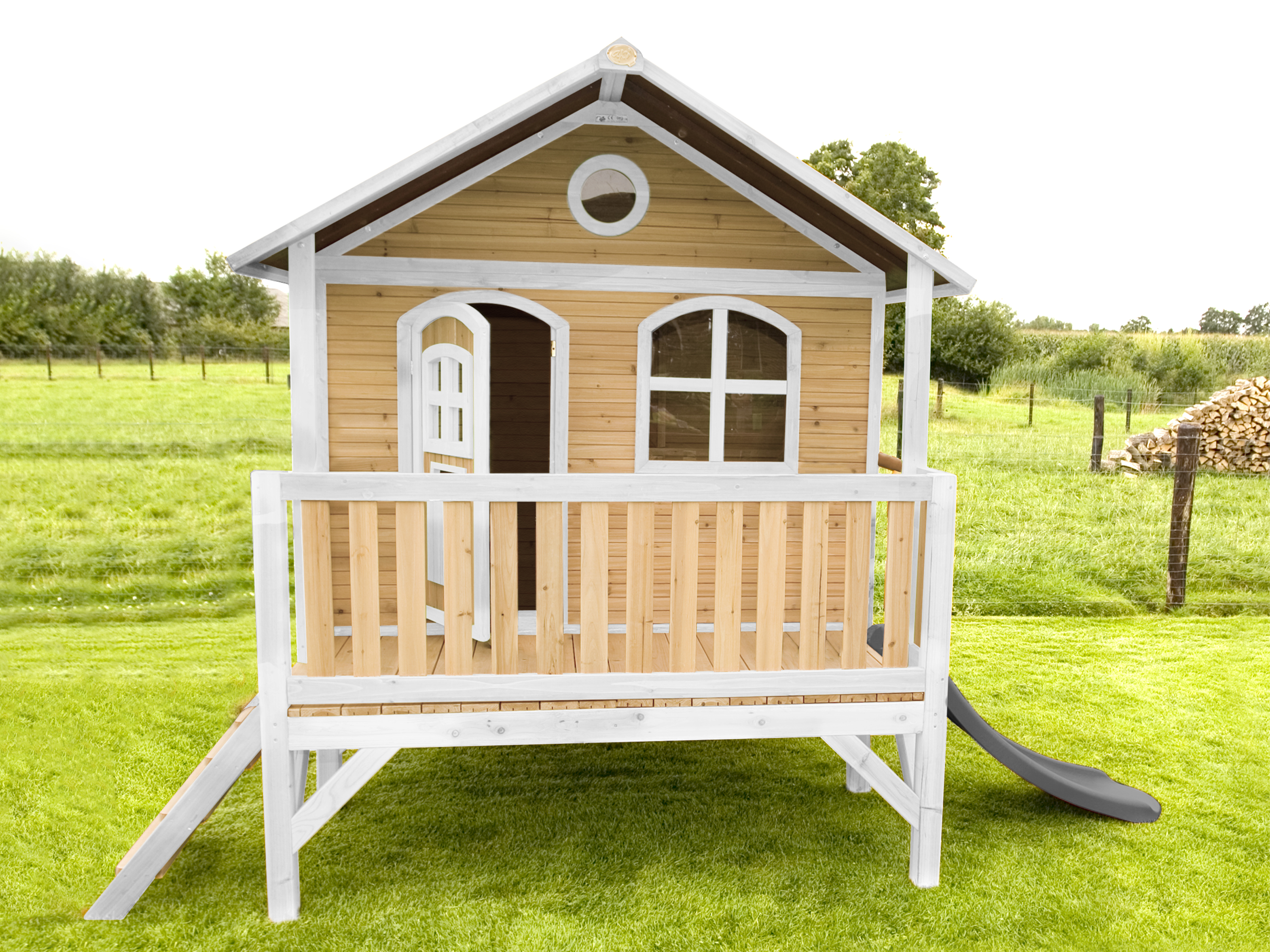 Ein Holzspielhaus mit Veranda, Rutsche und Rampe auf einer grünen Wiese.