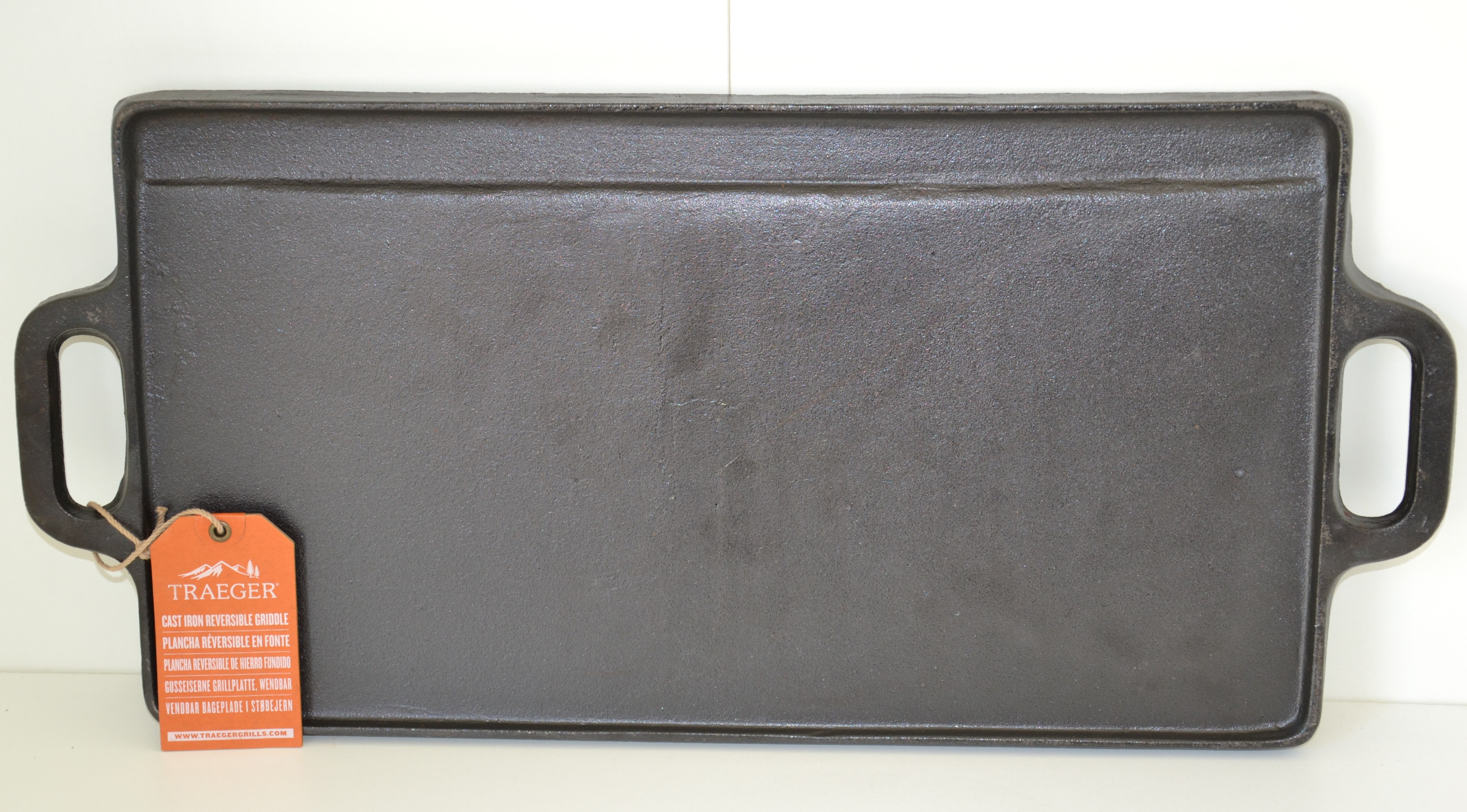 Una plancha rectangular de hierro fundido negra con dos asas y una etiqueta naranja.