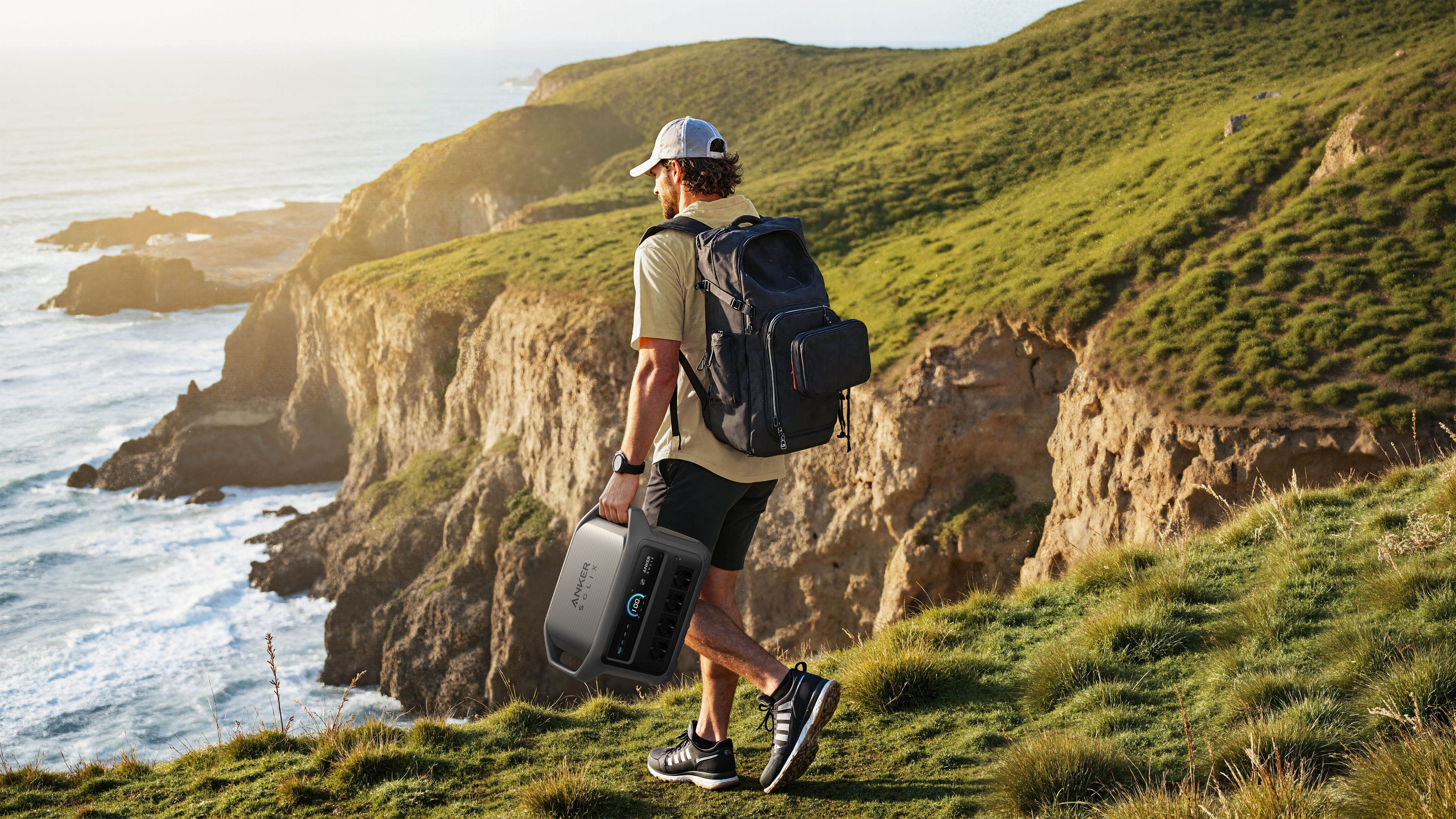 Mężczyzna z plecakiem niesie przenośną elektrownię wzdłuż skalistego wybrzeża.