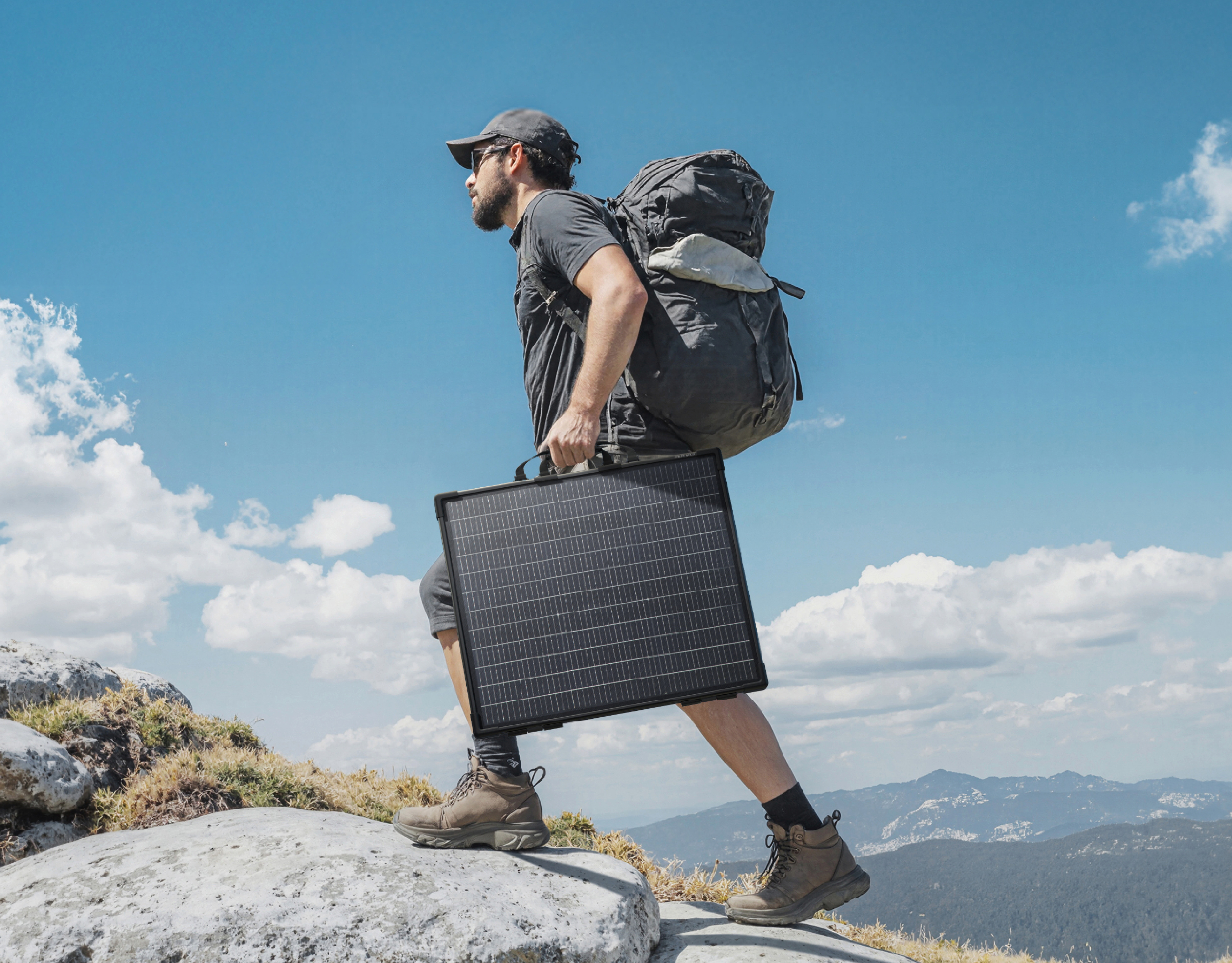 Mężczyzna z plecakiem i panelem słonecznym na górze, niebieskie niebo z chmurami.
