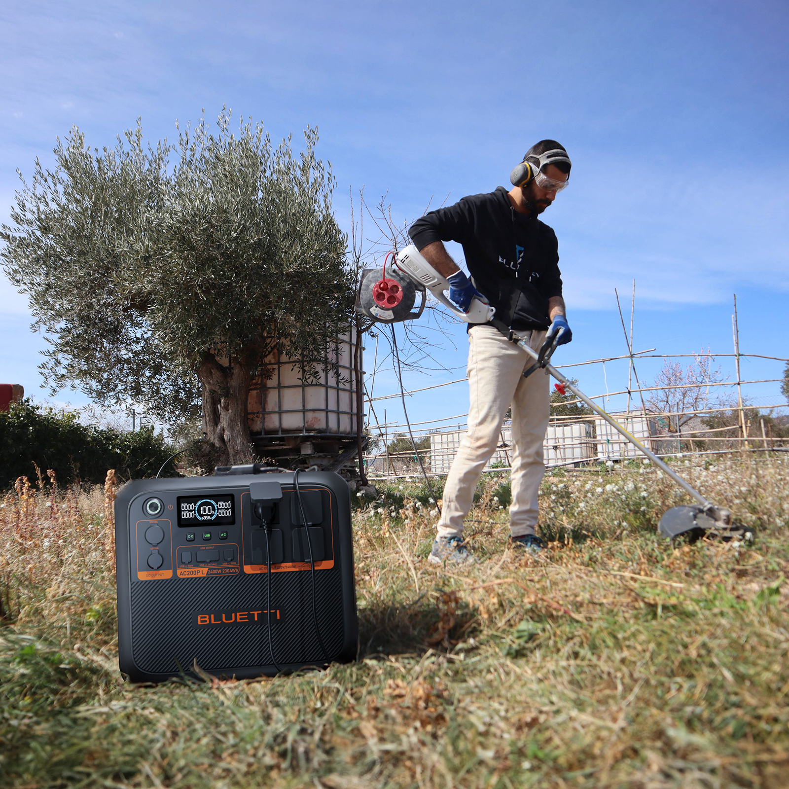 Mężczyzna kosi trawę podkaszarką obok power station pod błękitnym niebem.