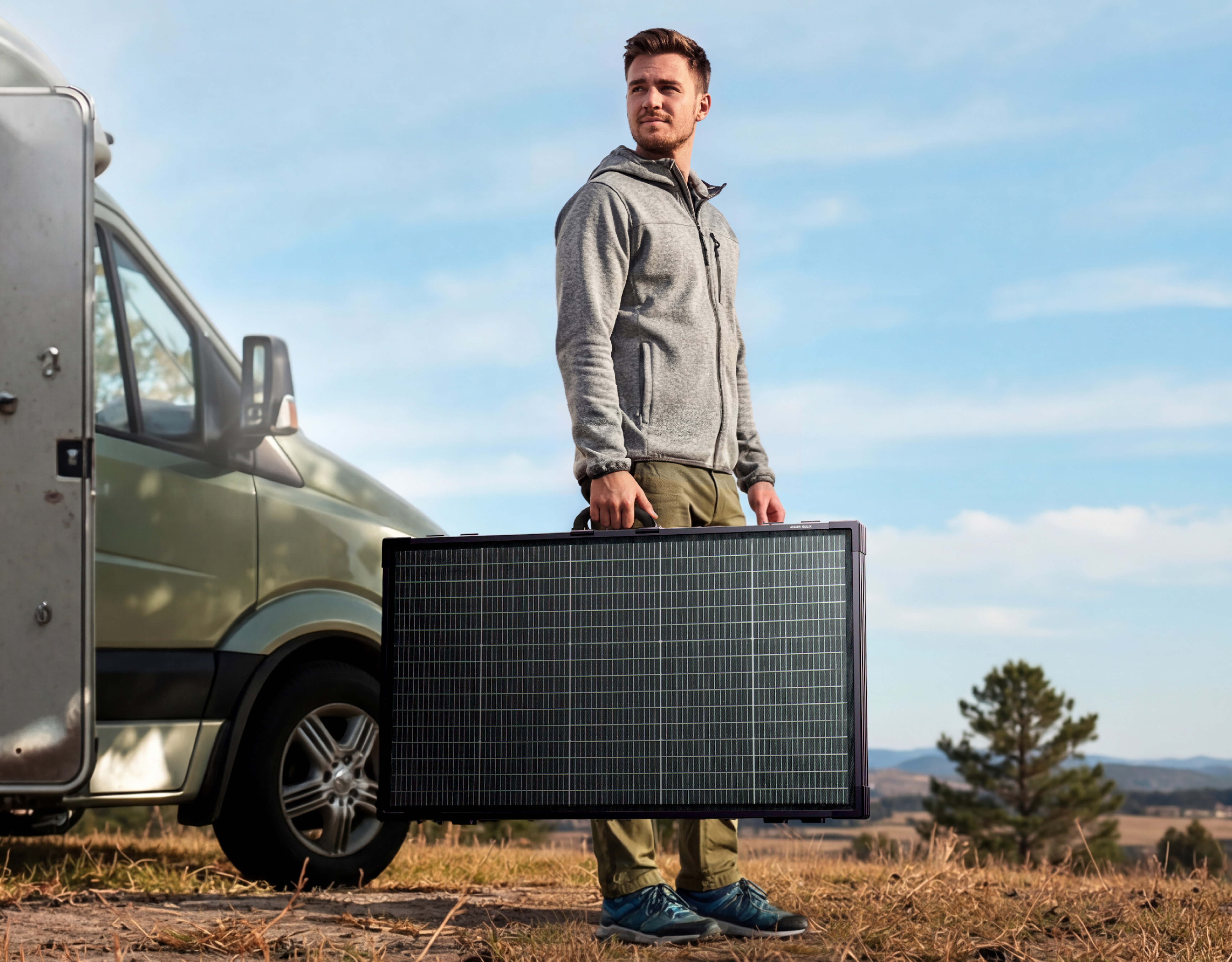 Mężczyzna z panelem słonecznym obok kampera na zewnątrz.